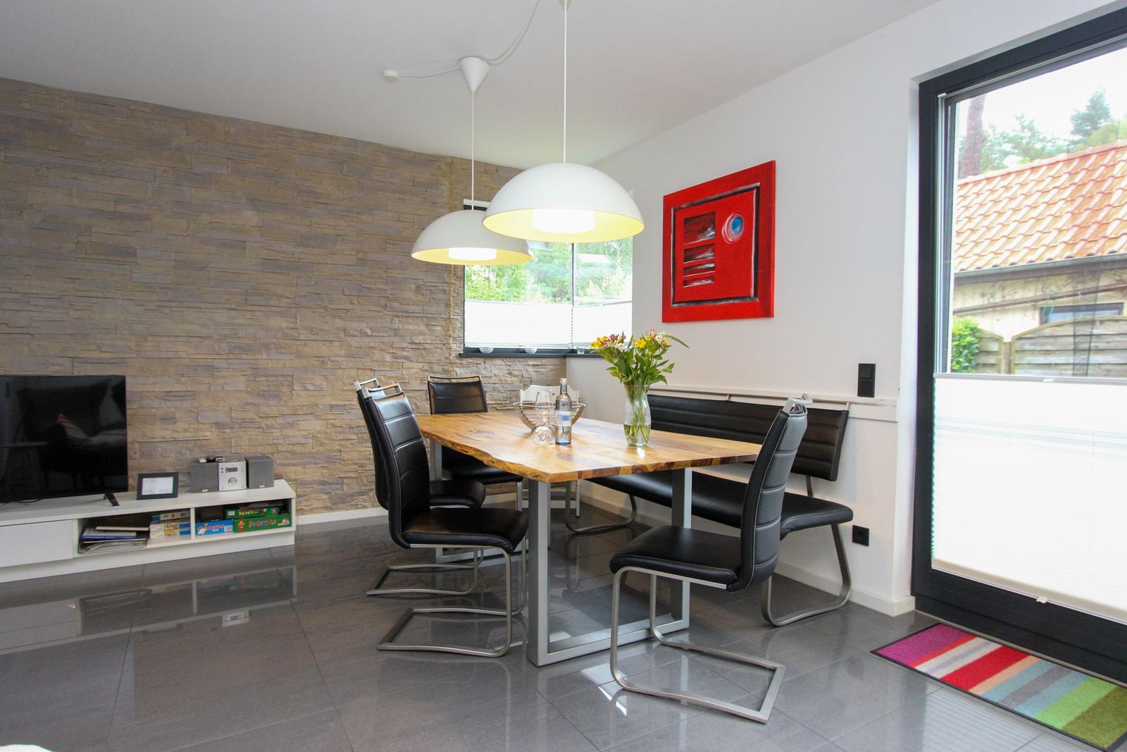 Essbereich mit Holztisch, schwarzen Stühlen und moderner Beleuchtung. Hintergrundwand aus Steinoptik.