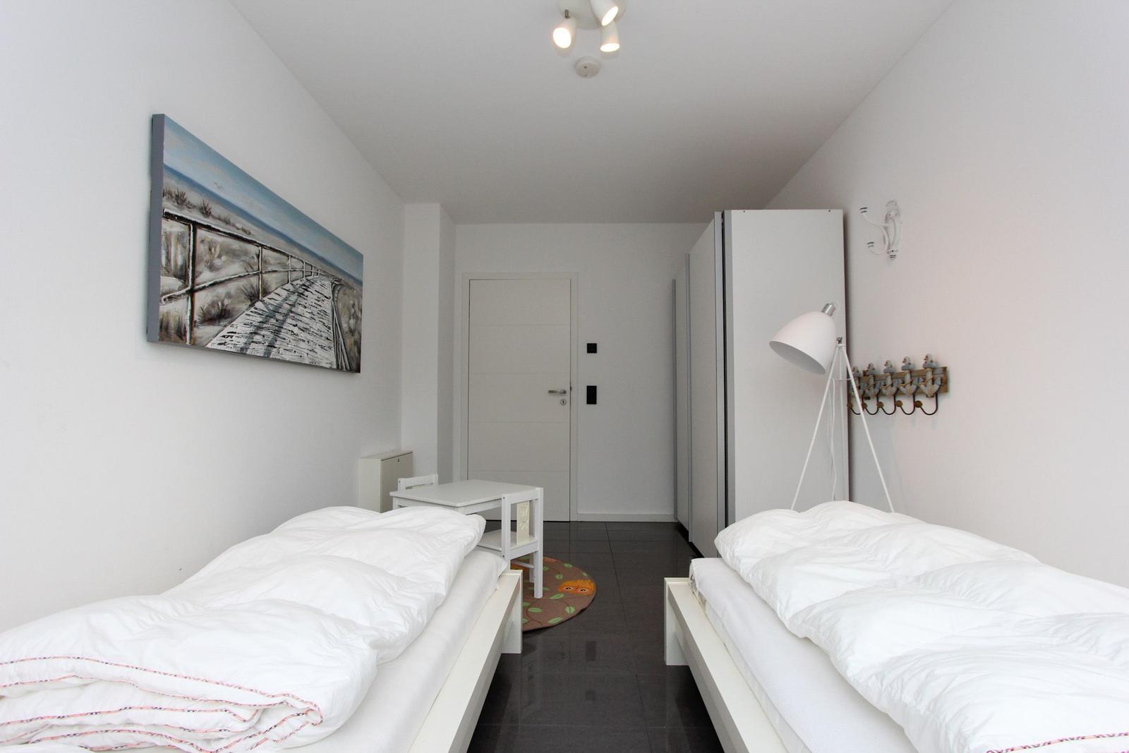 Zwei Betten, Wandbild, Schrank und Stehlampe im Schlafzimmer.