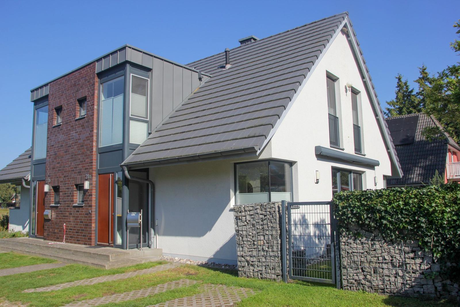 Moderne Villa mit Ziegelfassade und grauem Dach, umgeben von Grünfläche und Steinmauer.