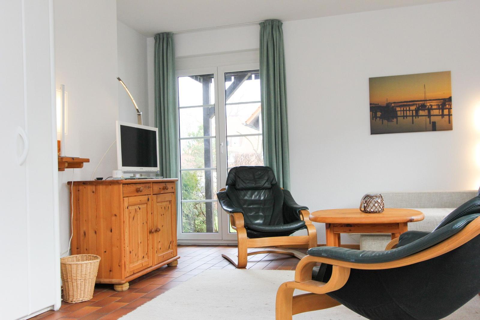 Wohnzimmer mit zwei schwarzen Ledersesseln, Holztisch und TV auf Holzschrank.