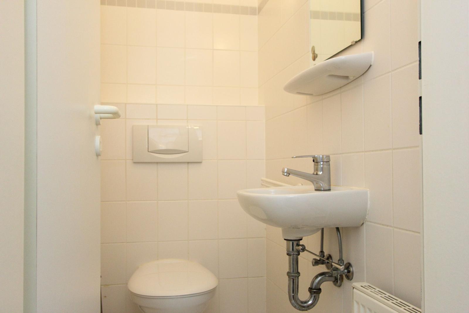 Badezimmer mit Toilette, Waschbecken und Spiegel an der Wand.