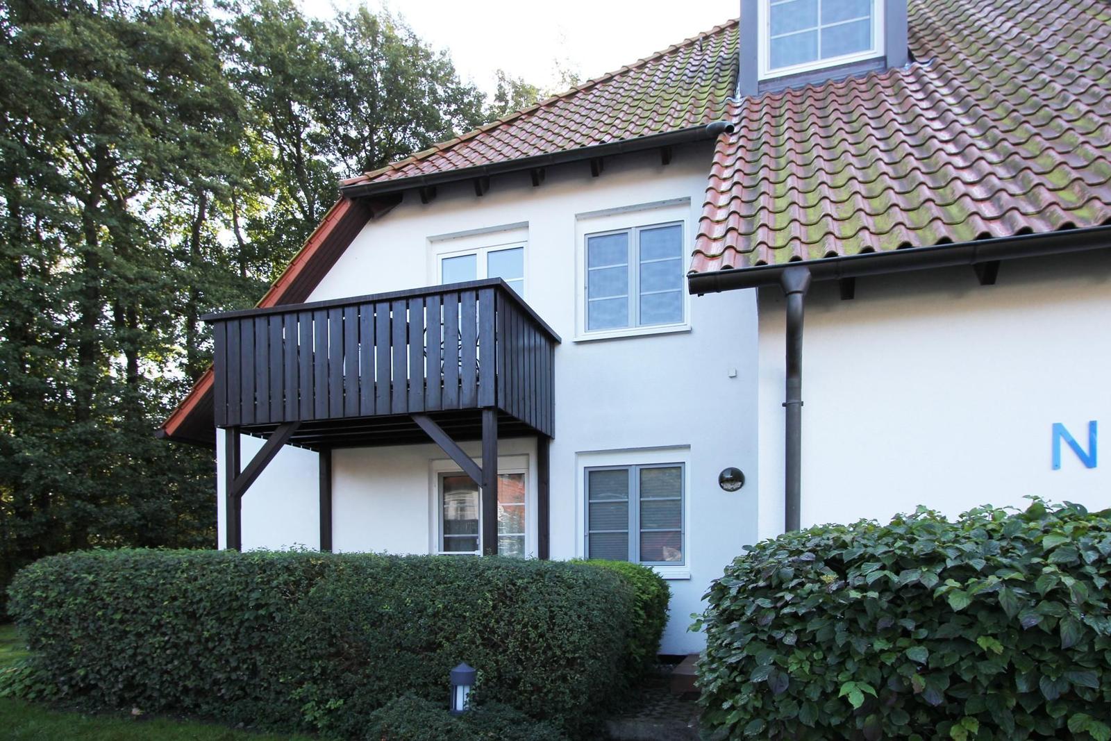 Weißes Haus mit Balkon, rotem Dach und grünen Hecken.