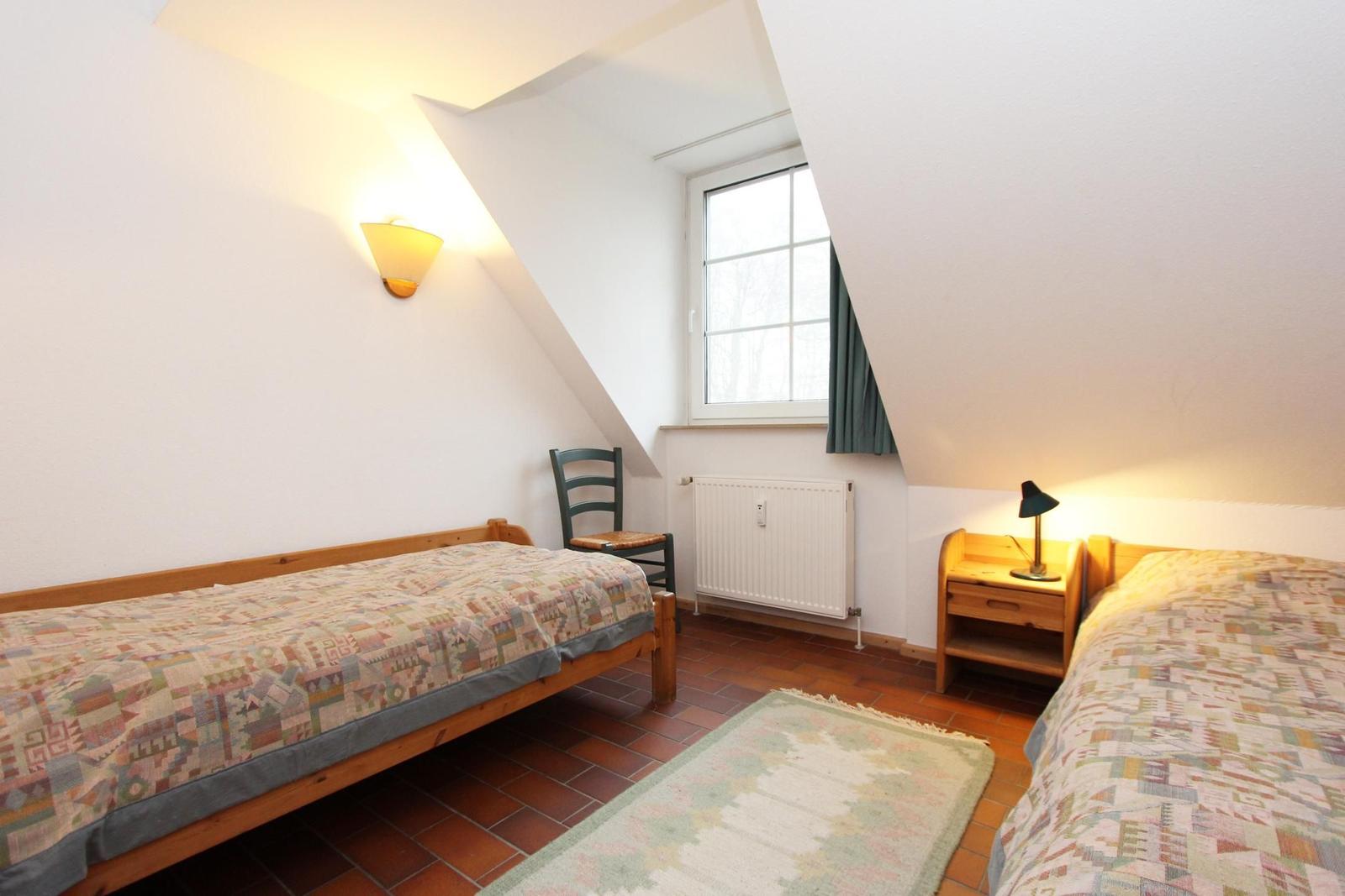 Zwei Betten, ein Fenster, eine Stehlampe und ein Schreibtisch im Dachzimmer.