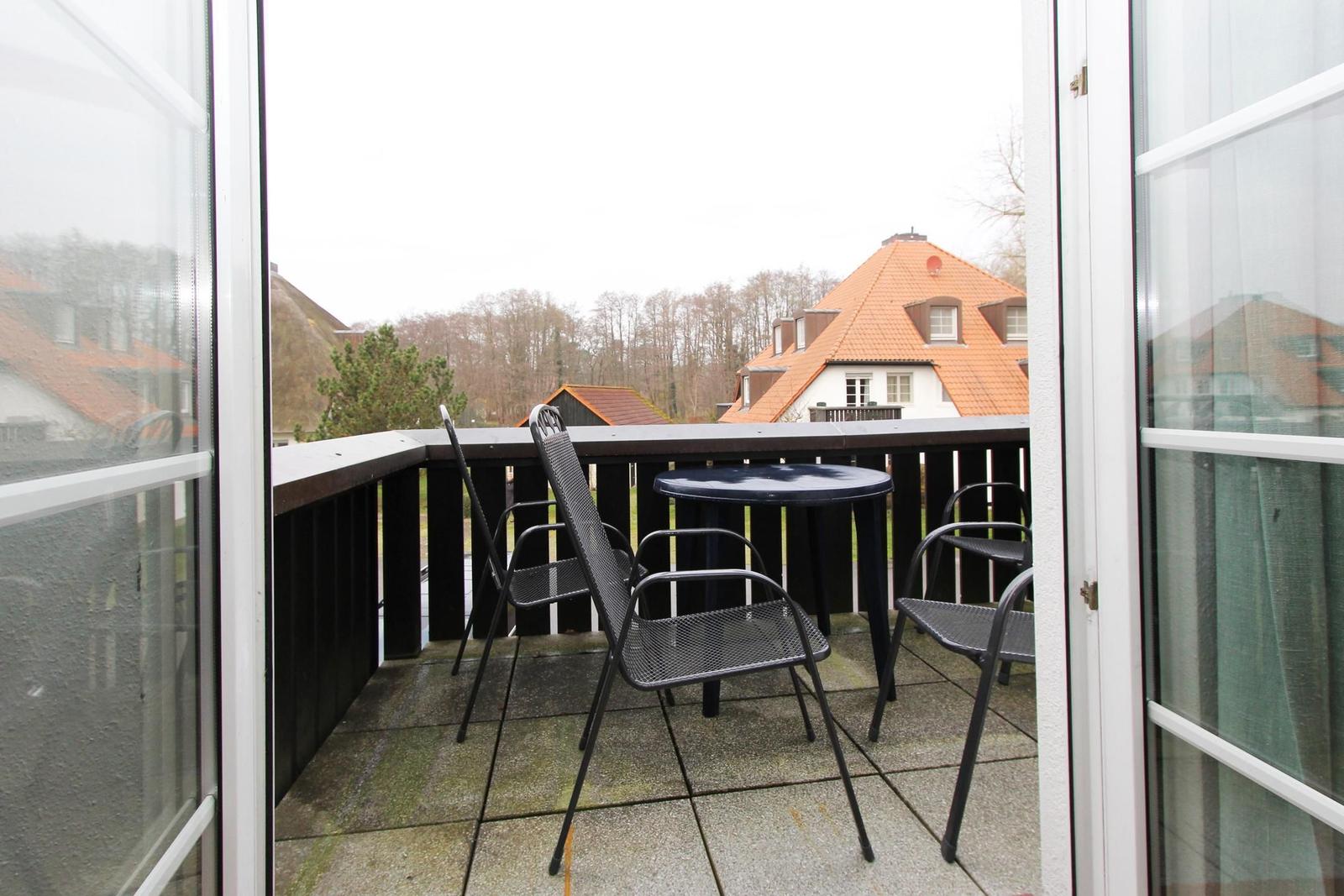 Terrasse mit Tisch und Stühlen, Blick auf Dächer und Bäume.
