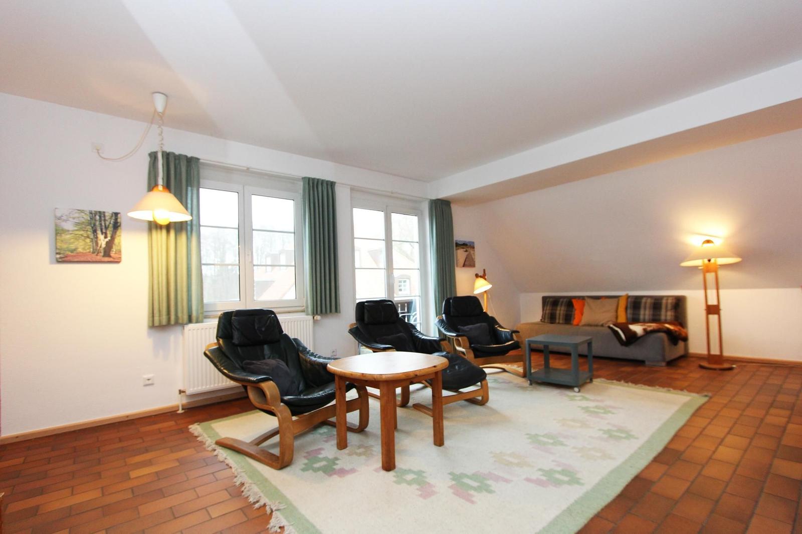 Wohnzimmer mit drei schwarzen Sesseln, Sofa, Tisch und Teppich auf Terrakottboden.