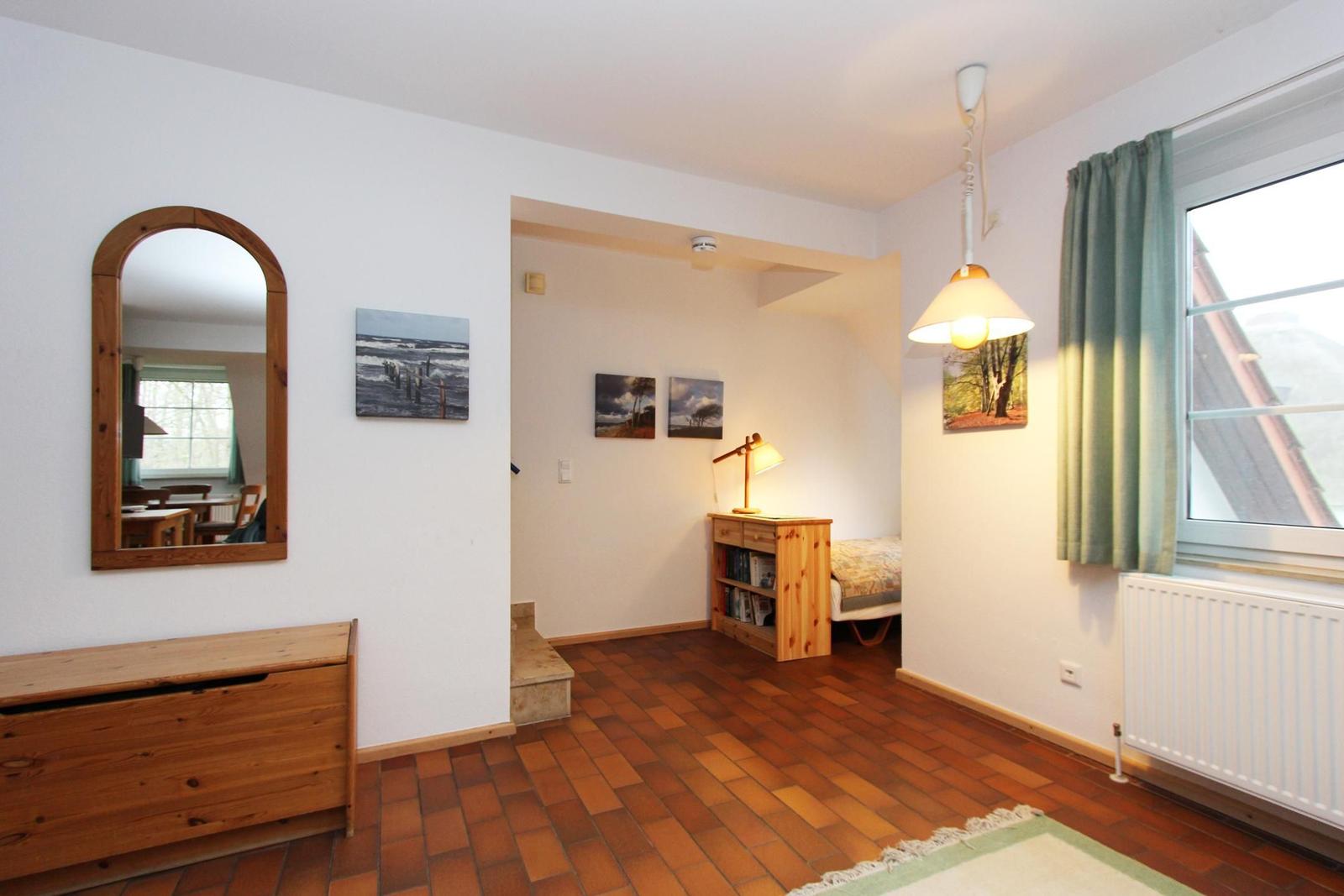 Zimmer mit Holzboden, Spiegel, Fenster und Bett im Hintergrund.