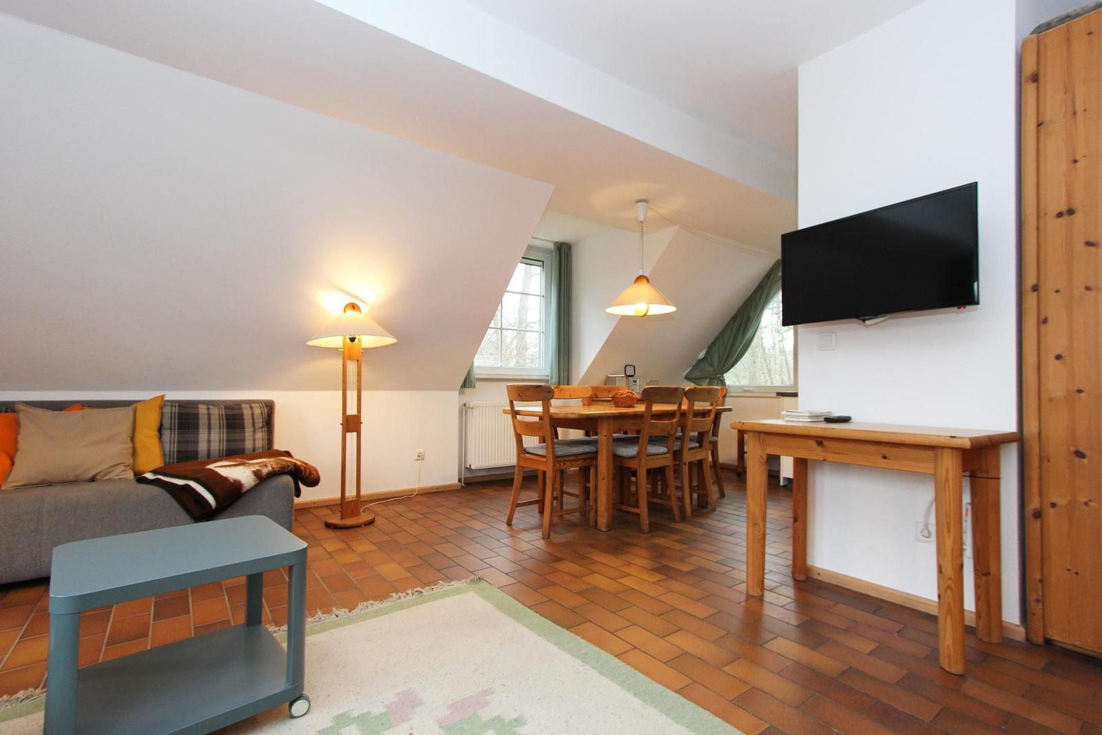 Wohn- und Essbereich mit Sofa, Esstisch, Fernseher und Holzboden.