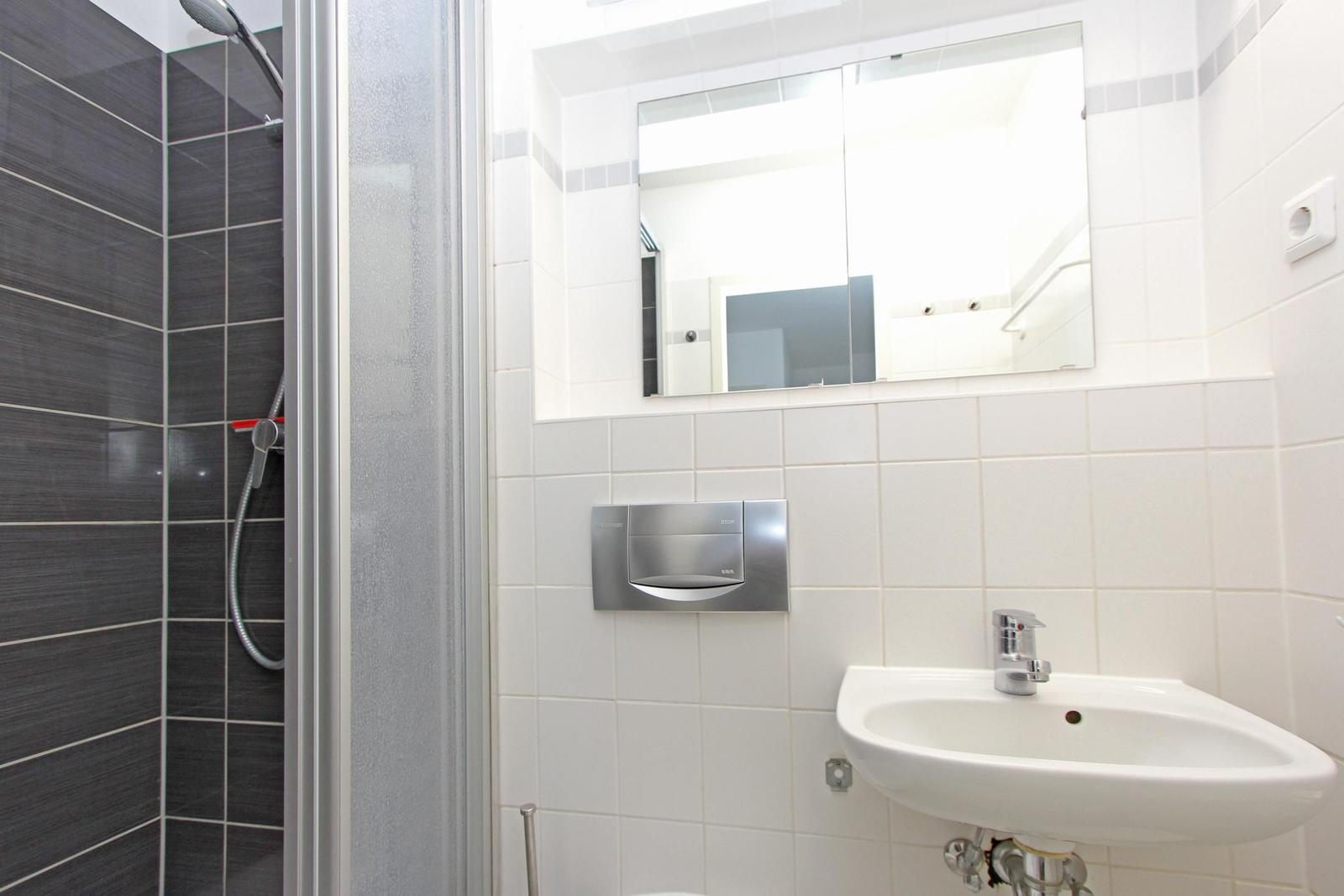 Badezimmer mit Dusche, Waschbecken und Spiegel.