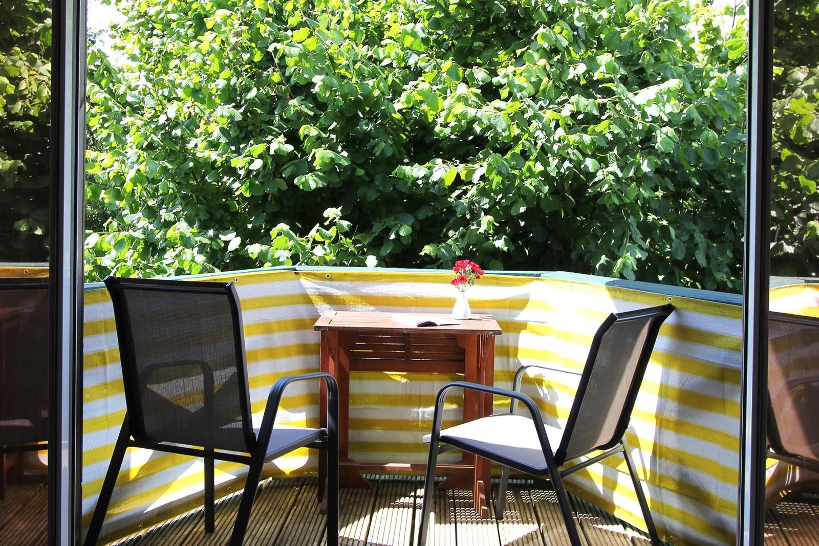 Terrasse mit zwei Stühlen und Tisch vor grüner Hecke.