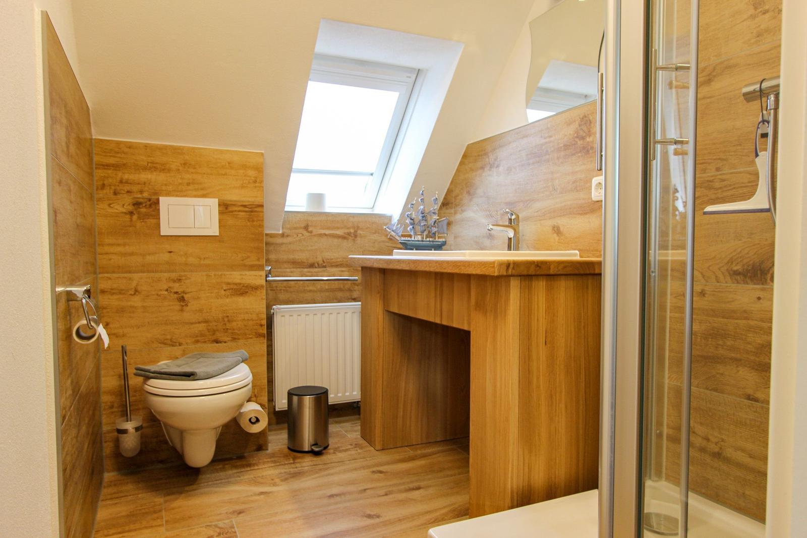 Badezimmer mit Holzwand, Toilette, Waschtisch und Dusche unter Dachschrägen.