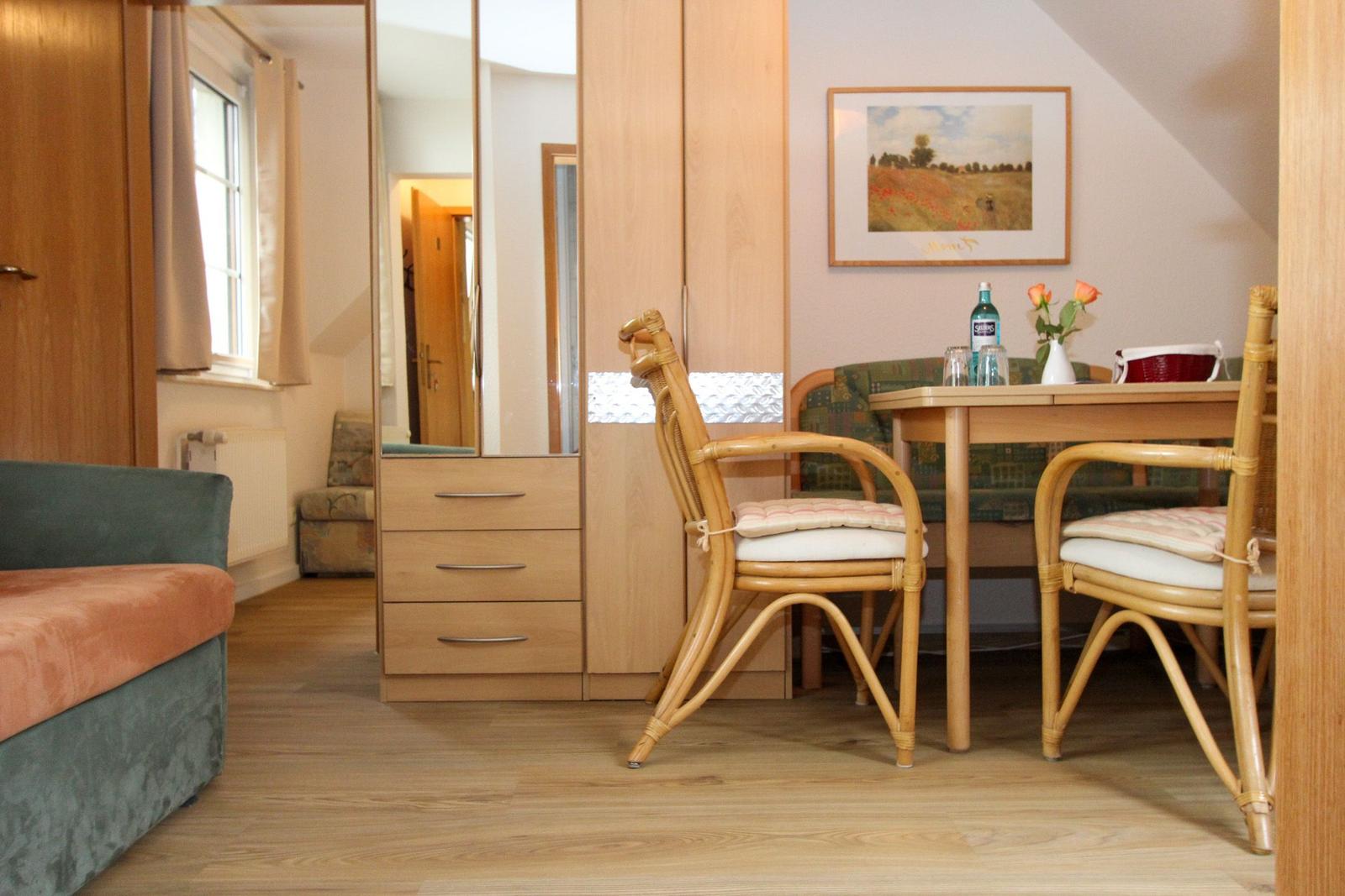 Ein Essbereich mit Holztisch, zwei Stühlen und einem Sofa im Hintergrund.