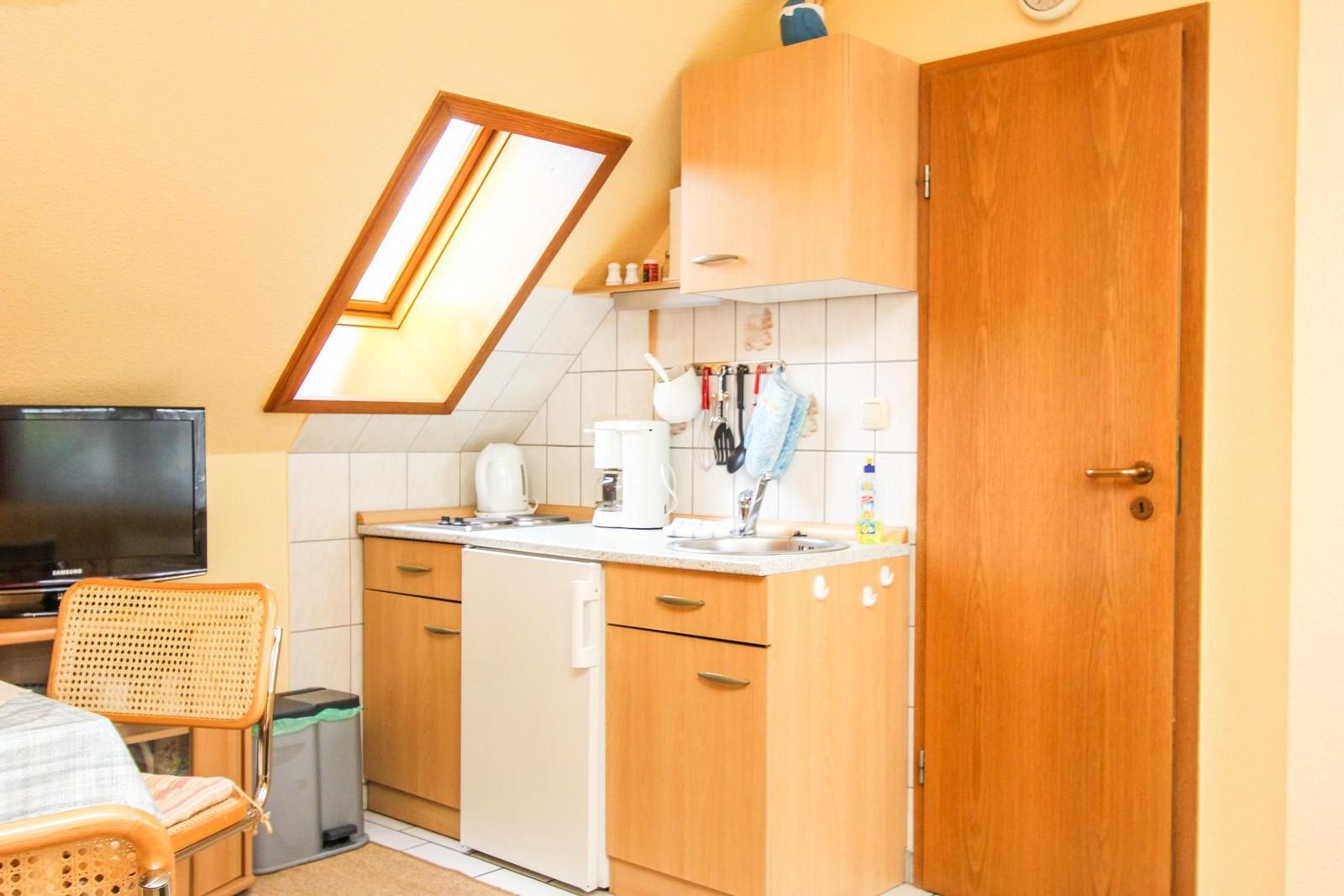 Küche mit Holzschränken, Spüle und Kühlschrank unter Dachschräge mit Dachfenster.