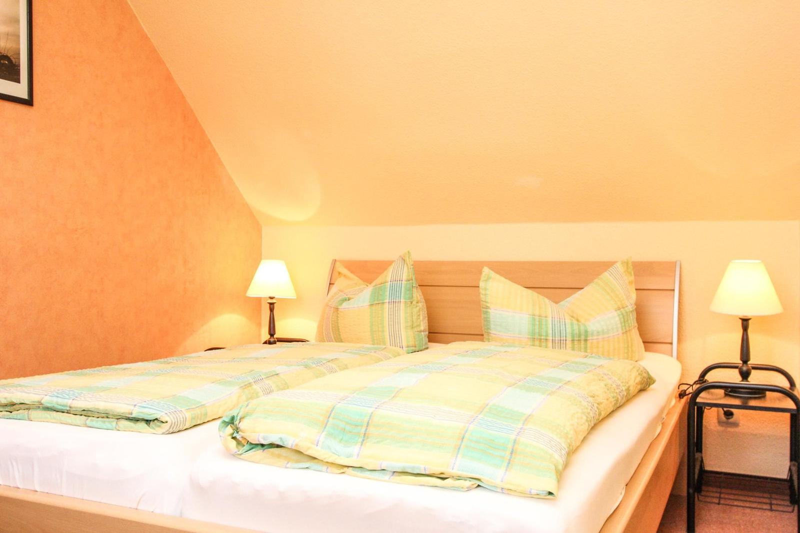 Ein Schlafzimmer mit Doppelbett, zwei Nachttischen und zwei Lampen. Die Wände sind orange und weiß gestrichen.