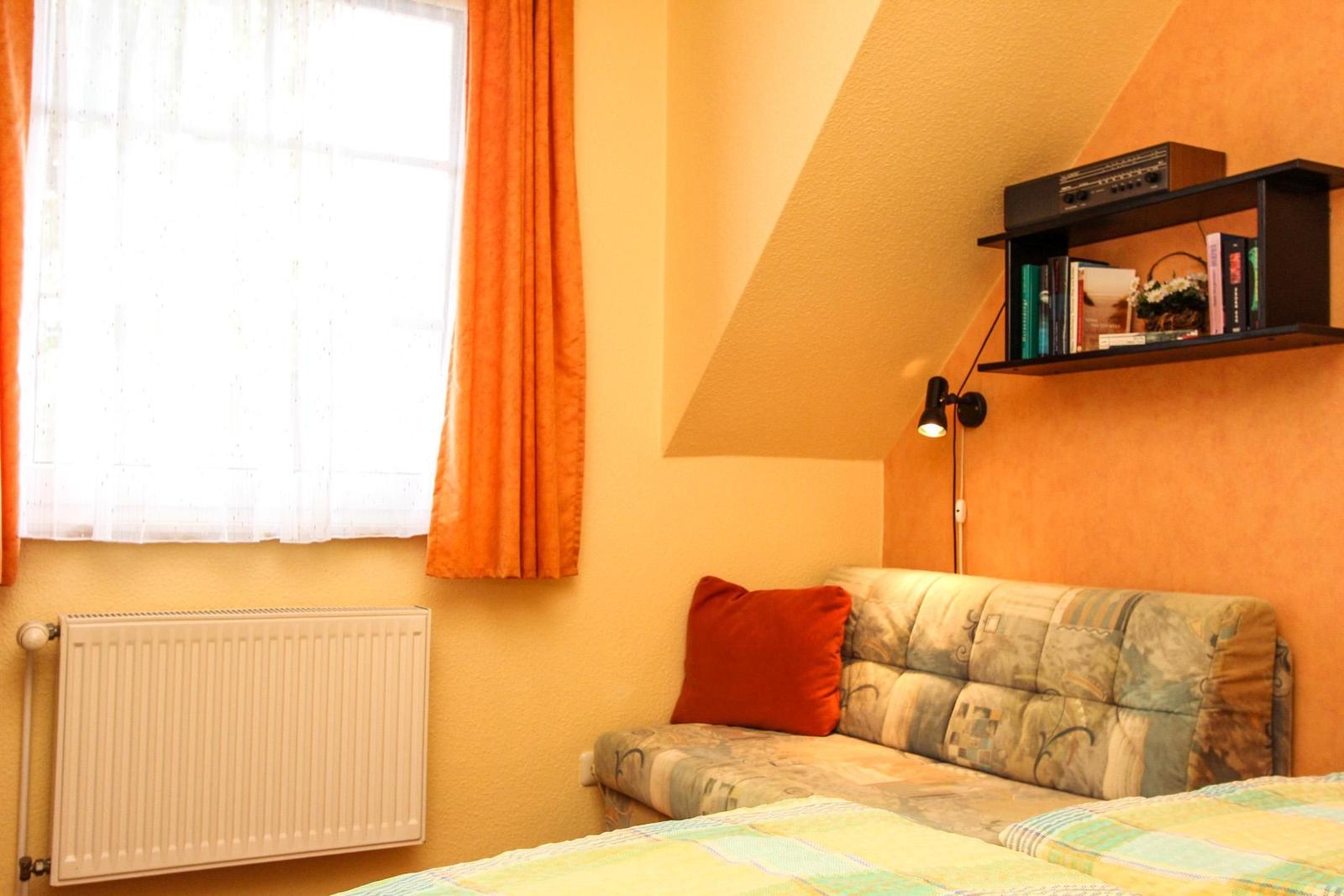 Schlafzimmer mit Bett, Sofa und Fenster mit Vorhängen.
