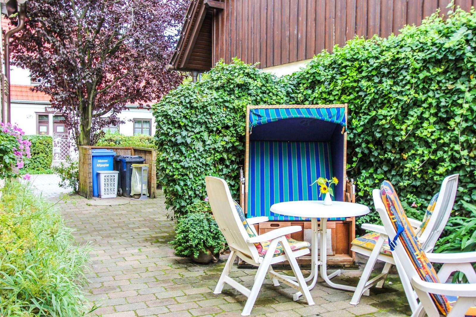 Terrasse mit Strandkorb, Tisch und Stühlen vor grüner Hecke.