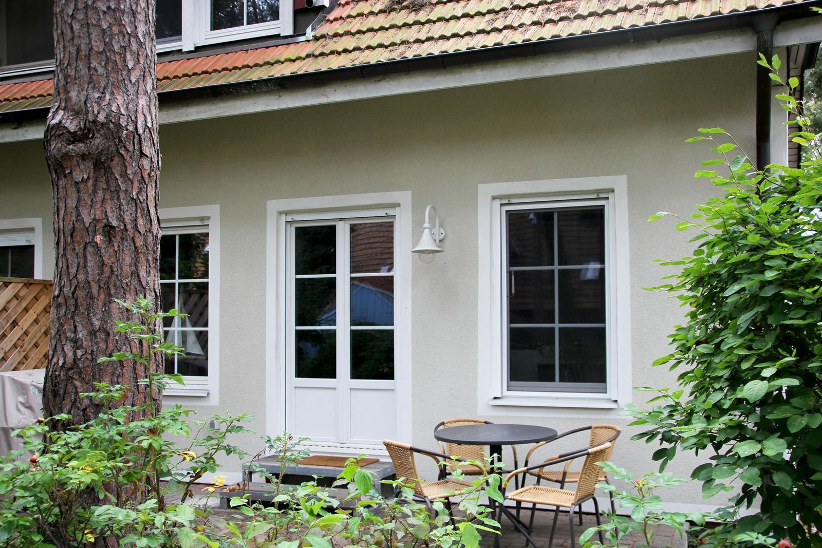 Haus mit Terrasse, Tisch und Stühlen, umgeben von Bäumen und Sträuchern.