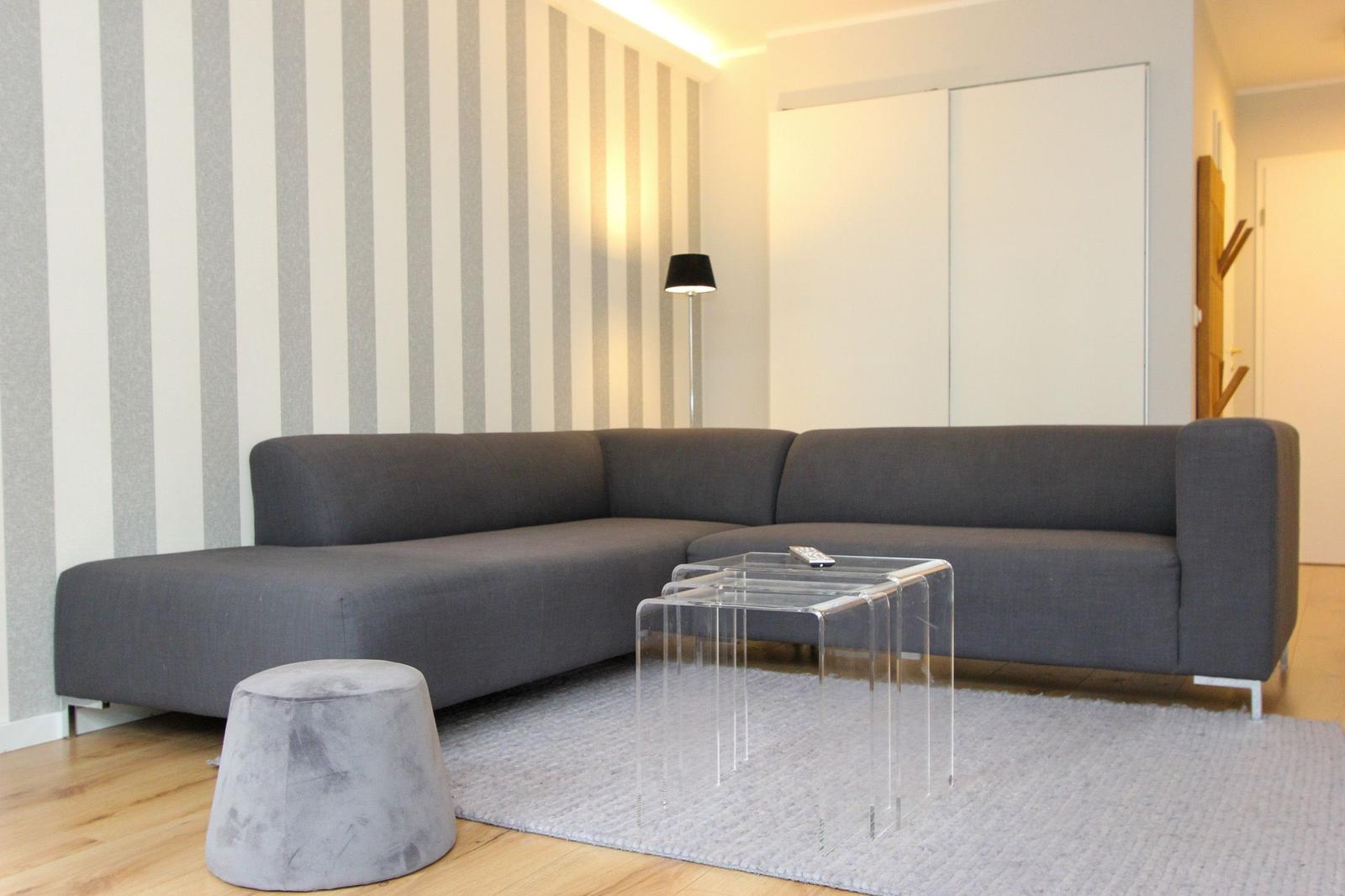 Ein Wohnzimmer mit grauem Sofa, transparentem Tisch und gestreifter Wand.