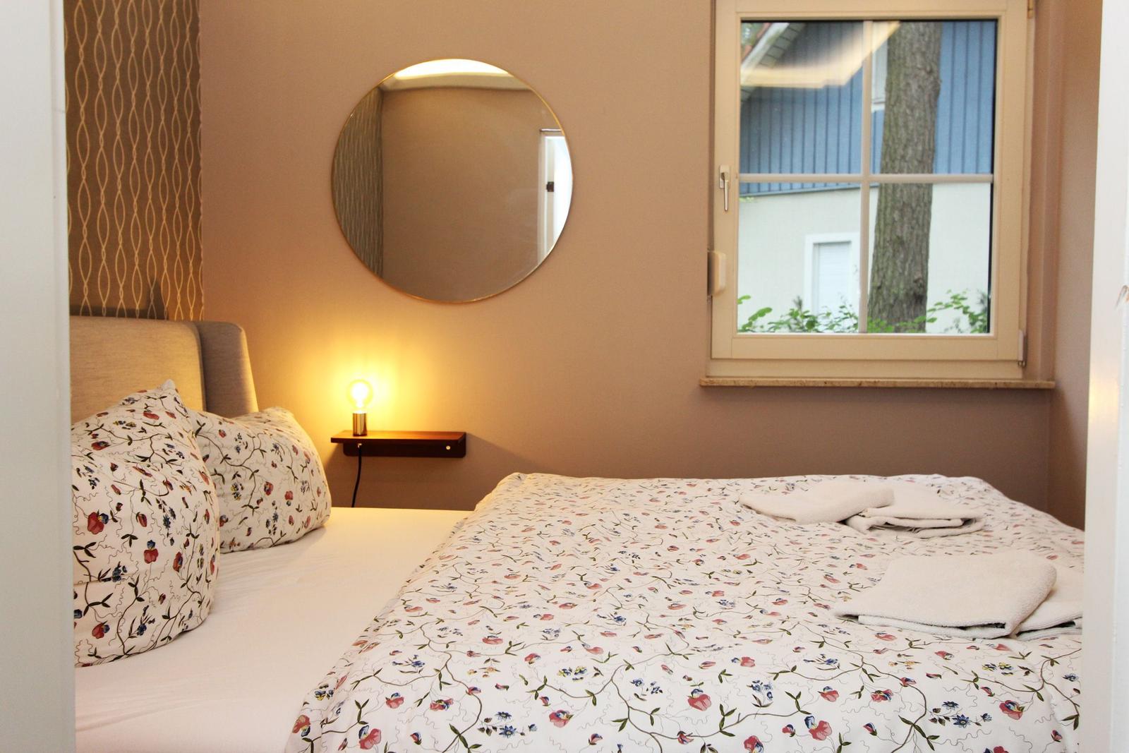 Ein Schlafzimmer mit Bett, Spiegel und Fenster. Auf dem Bett liegen Handtücher.