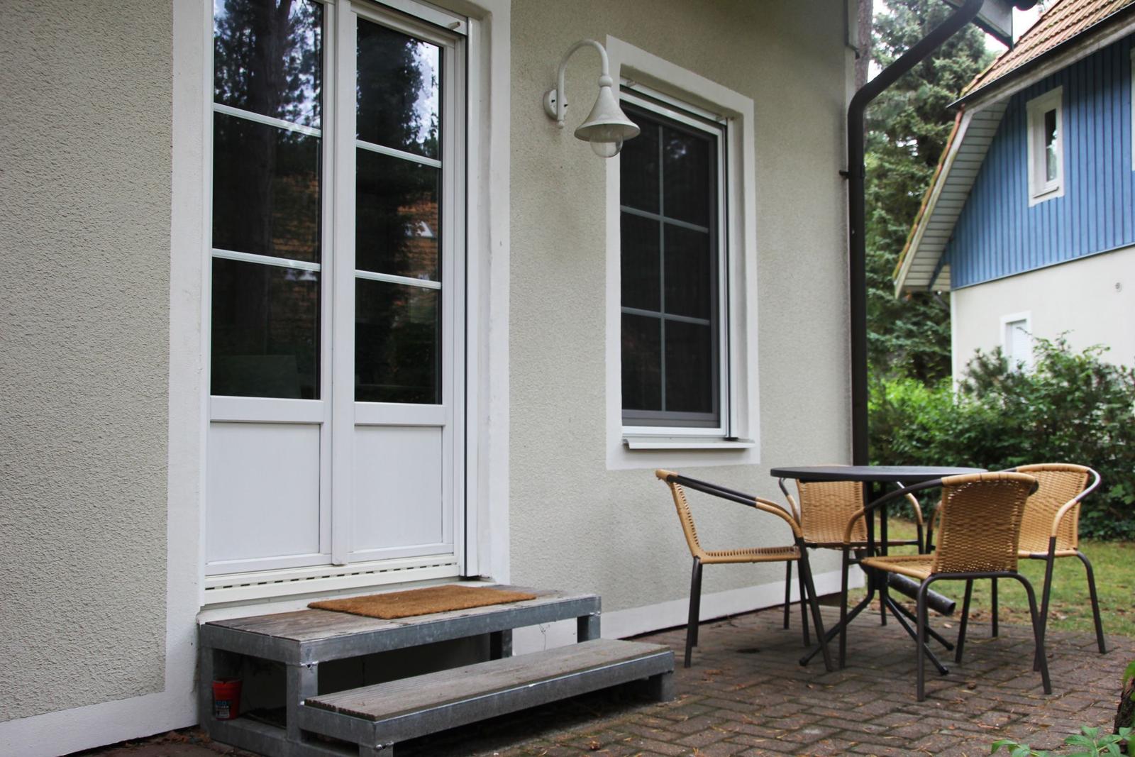 Terrasse mit Tisch und Stühlen vor einer Haustür mit Fenstern.