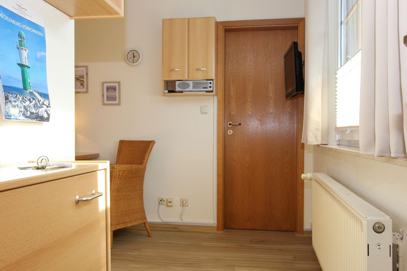 Kleines Zimmer mit Holztür, Schrank, Stuhl und Fenster mit Vorhang.