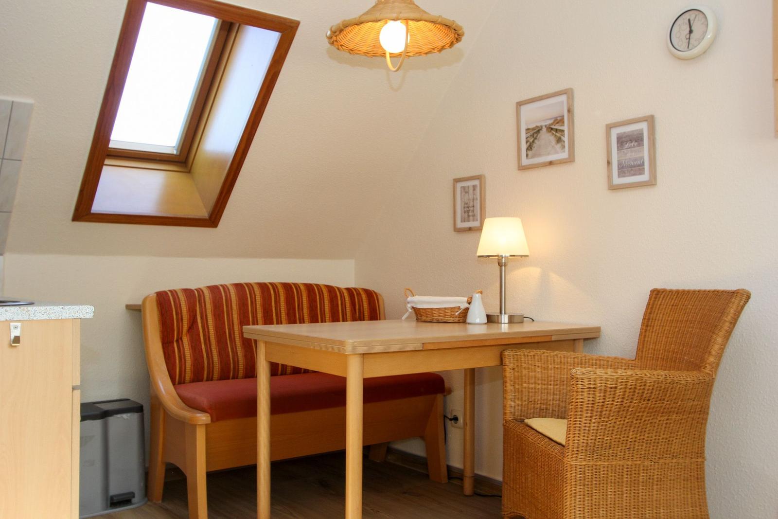 Esstisch mit Bänken und Stuhl unter Dachschräge mit Fenster und Lampe.