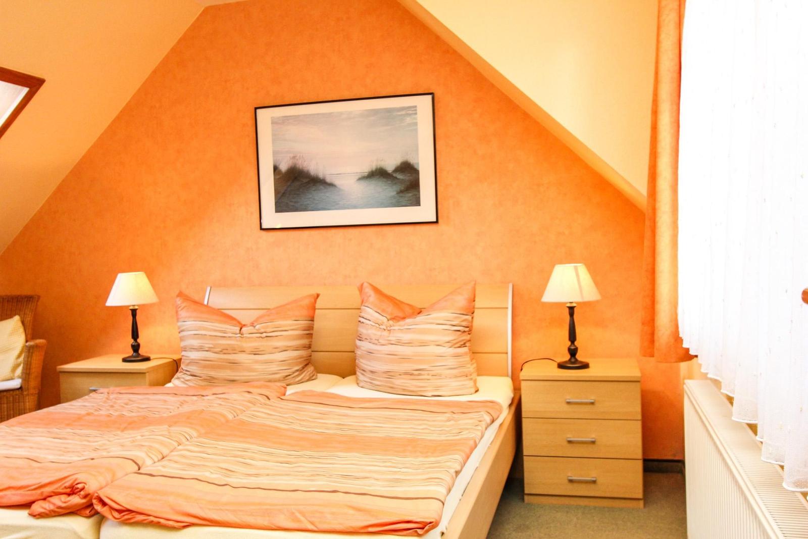 Schlafzimmer mit Dachschrägen, Bett, Nachttischen und Bild an der Wand.