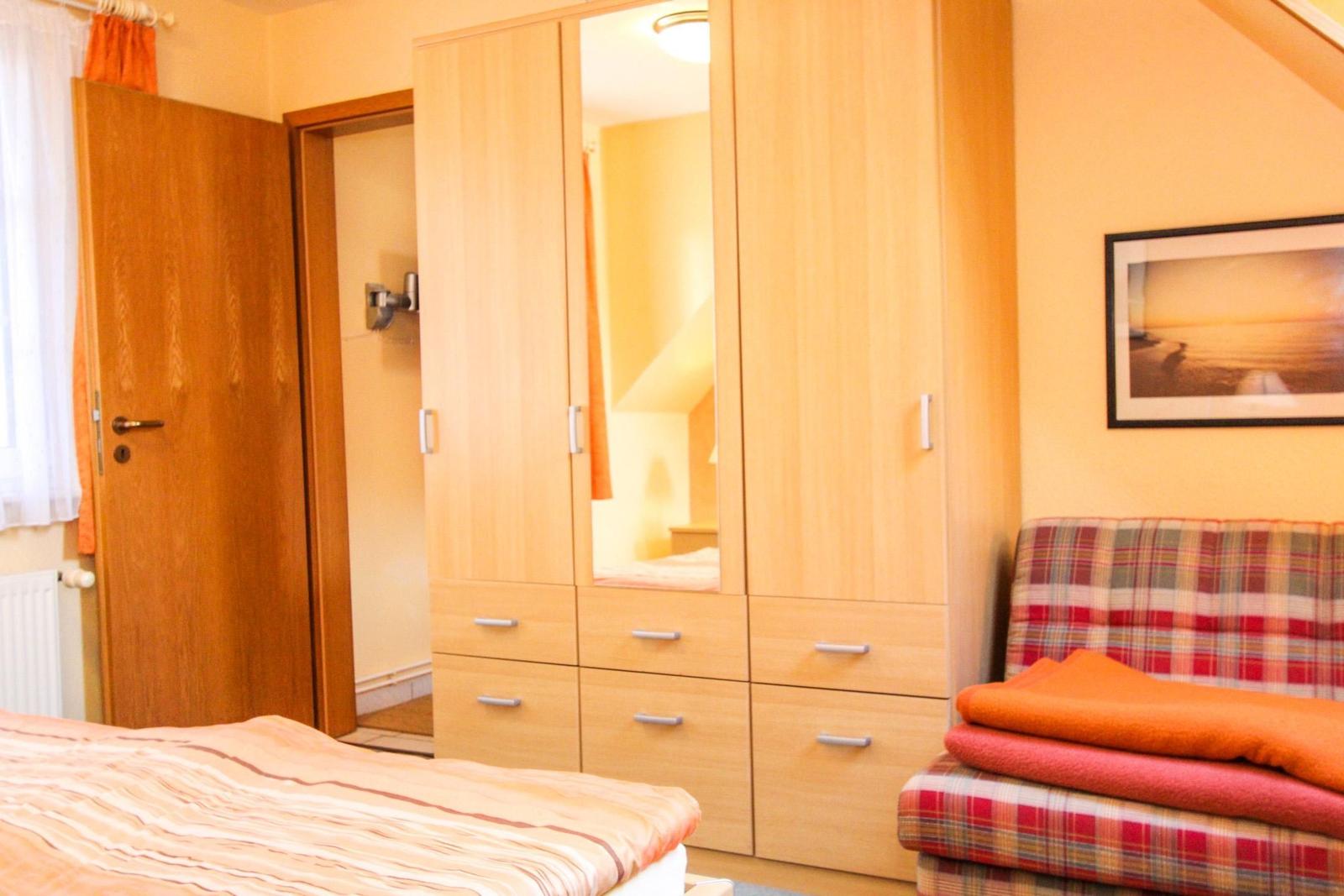 Schlafzimmer mit Bett, Kleiderschrank und Sitzbank mit Decke.