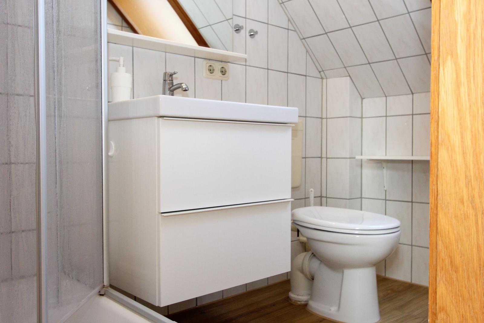 Badezimmer mit Waschbecken, Toilette und Dusche unter Dachschrägen.