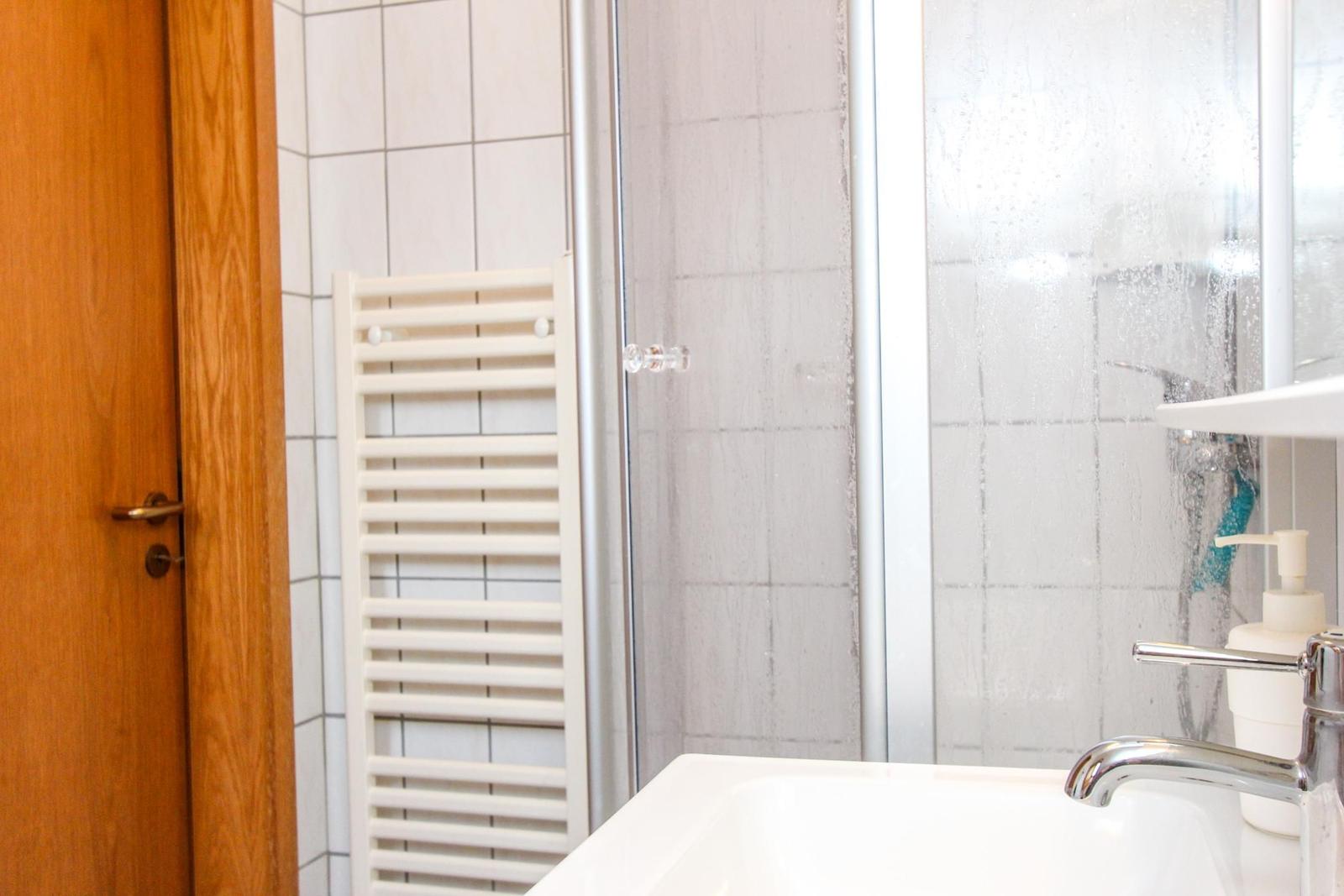 Bad mit Dusche, Waschbecken und Heizkörper an der Wand.