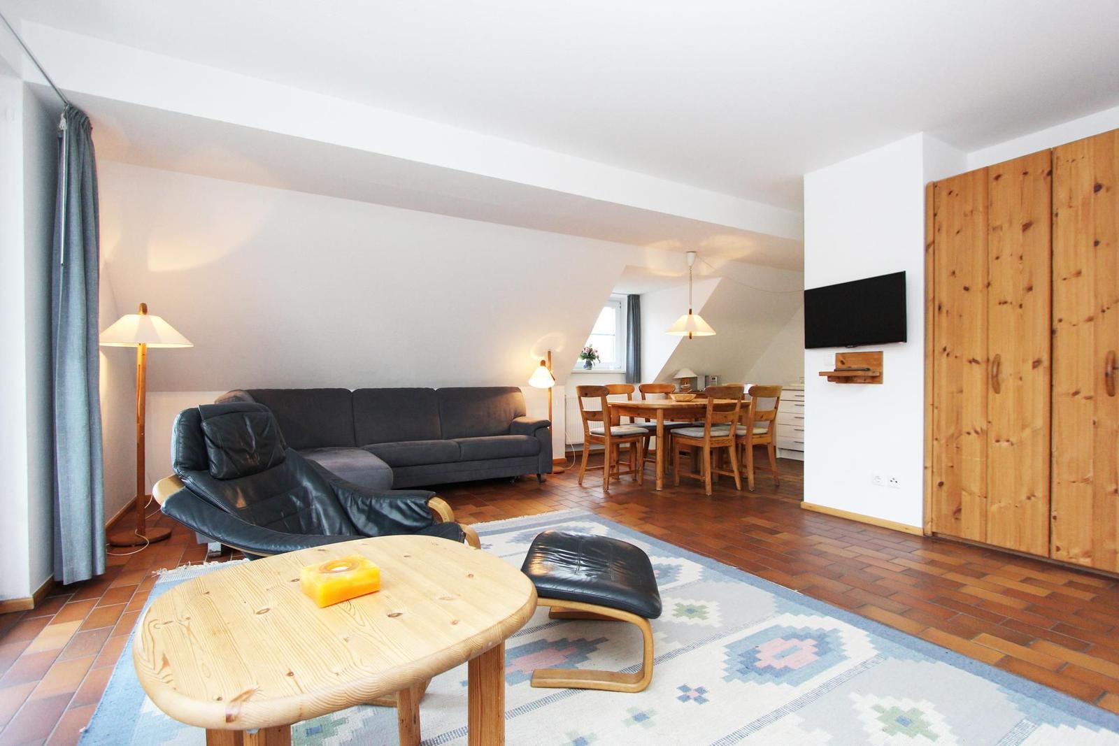 Wohn- und Essbereich mit Sofa, Esstisch und Fernseher an der Wand.