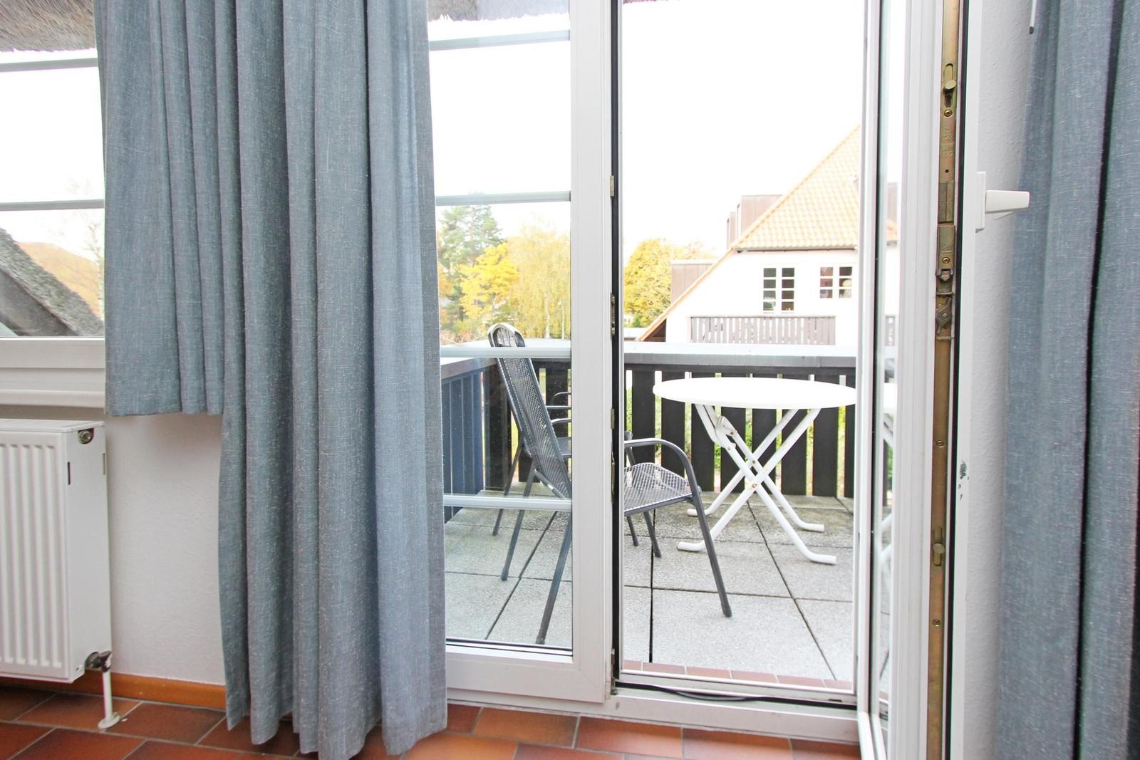 Durch die Glastür ist eine Terrasse mit Tisch und Stühlen sichtbar.