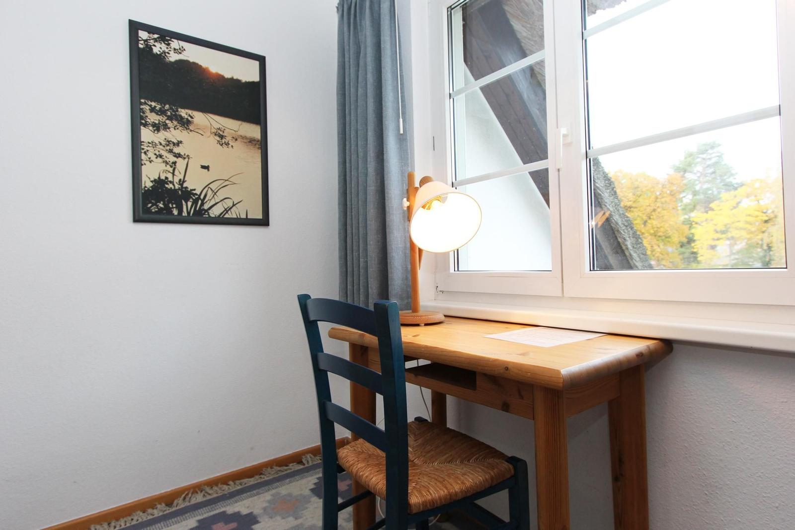 Schreibtisch mit Stuhl unter Fenster, Wandbild und Lampe.