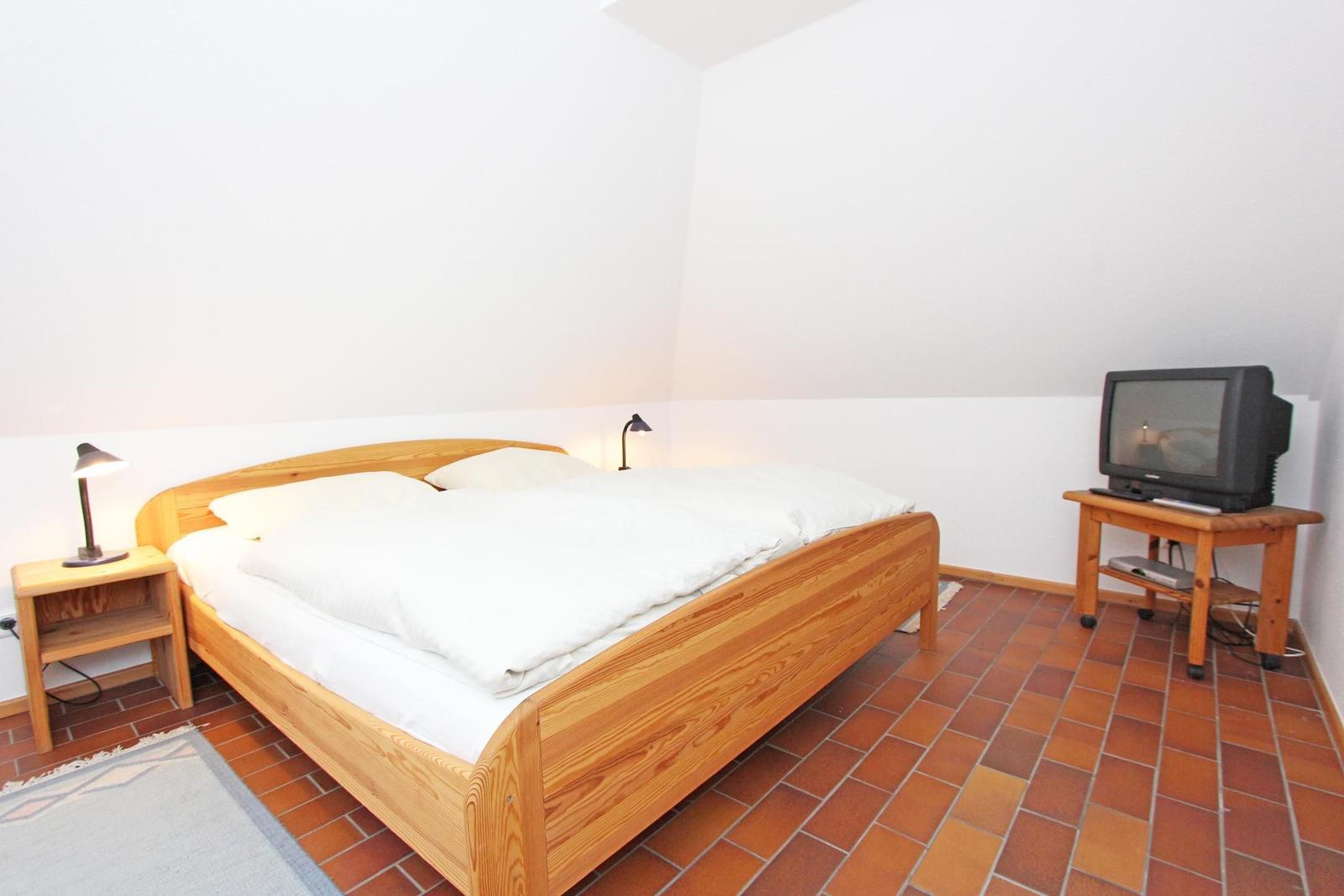 Schlafzimmer mit Holzbett, Nachttisch und Fernseher auf Holzständer.