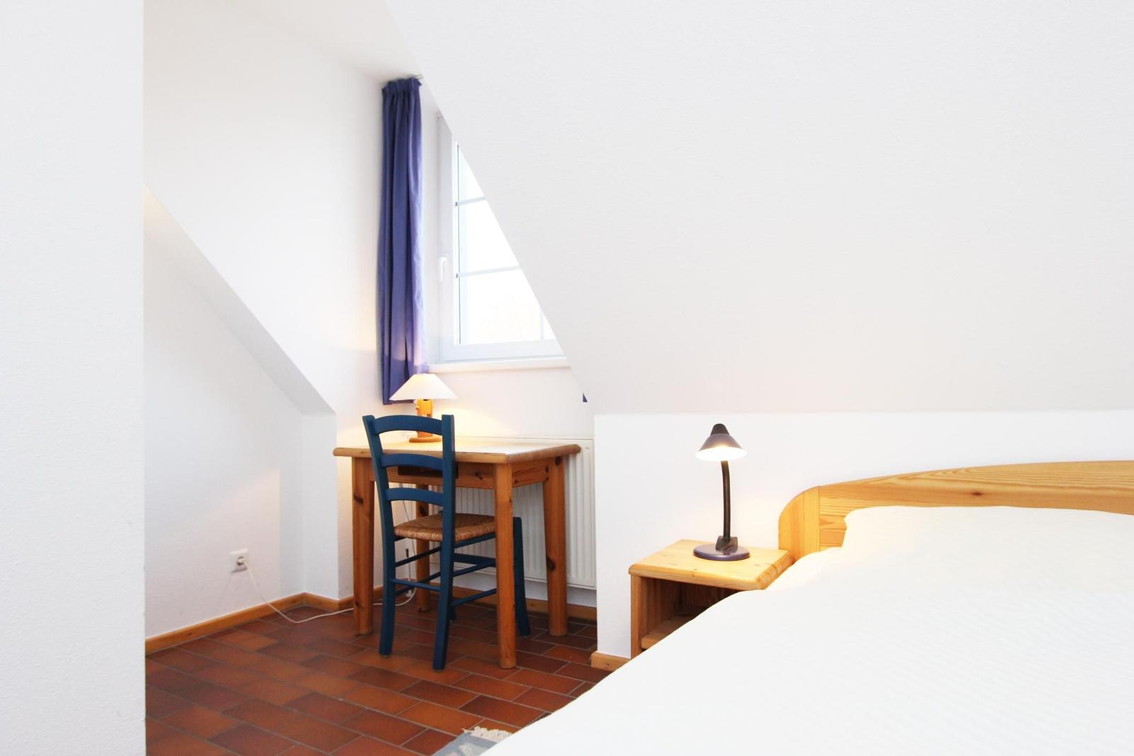 Schlafzimmer mit Bett, Schreibtisch und Fenster unter Dachschräge.
