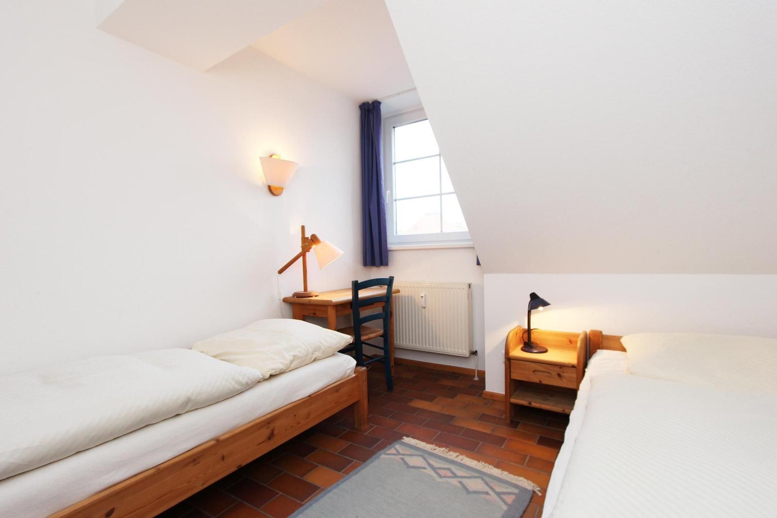 Zwei Betten, Schreibtisch, Fenster und Nachttisch mit Lampe.