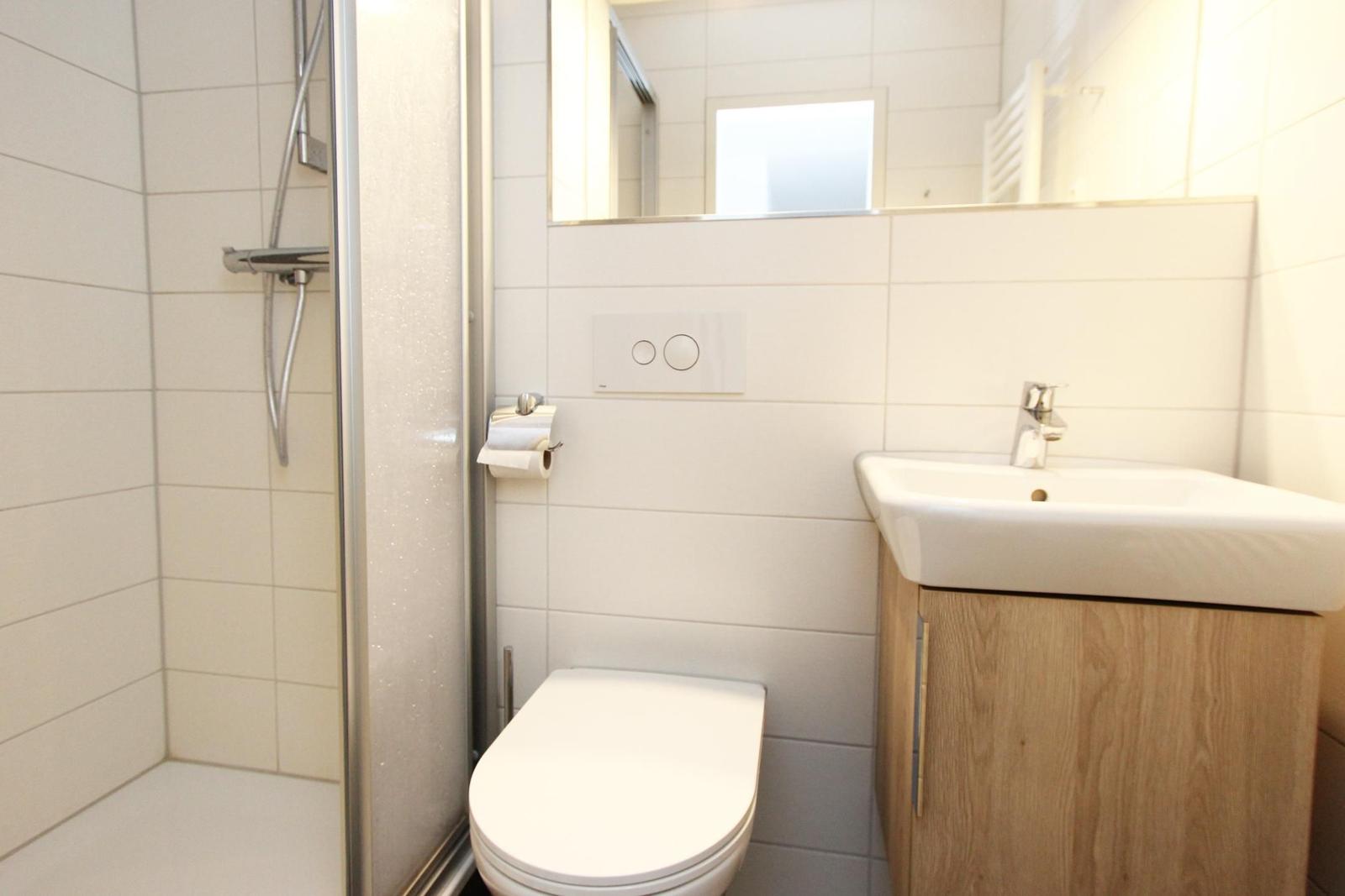Badezimmer mit Dusche, Toilette und Waschbecken mit Holzunterschrank.