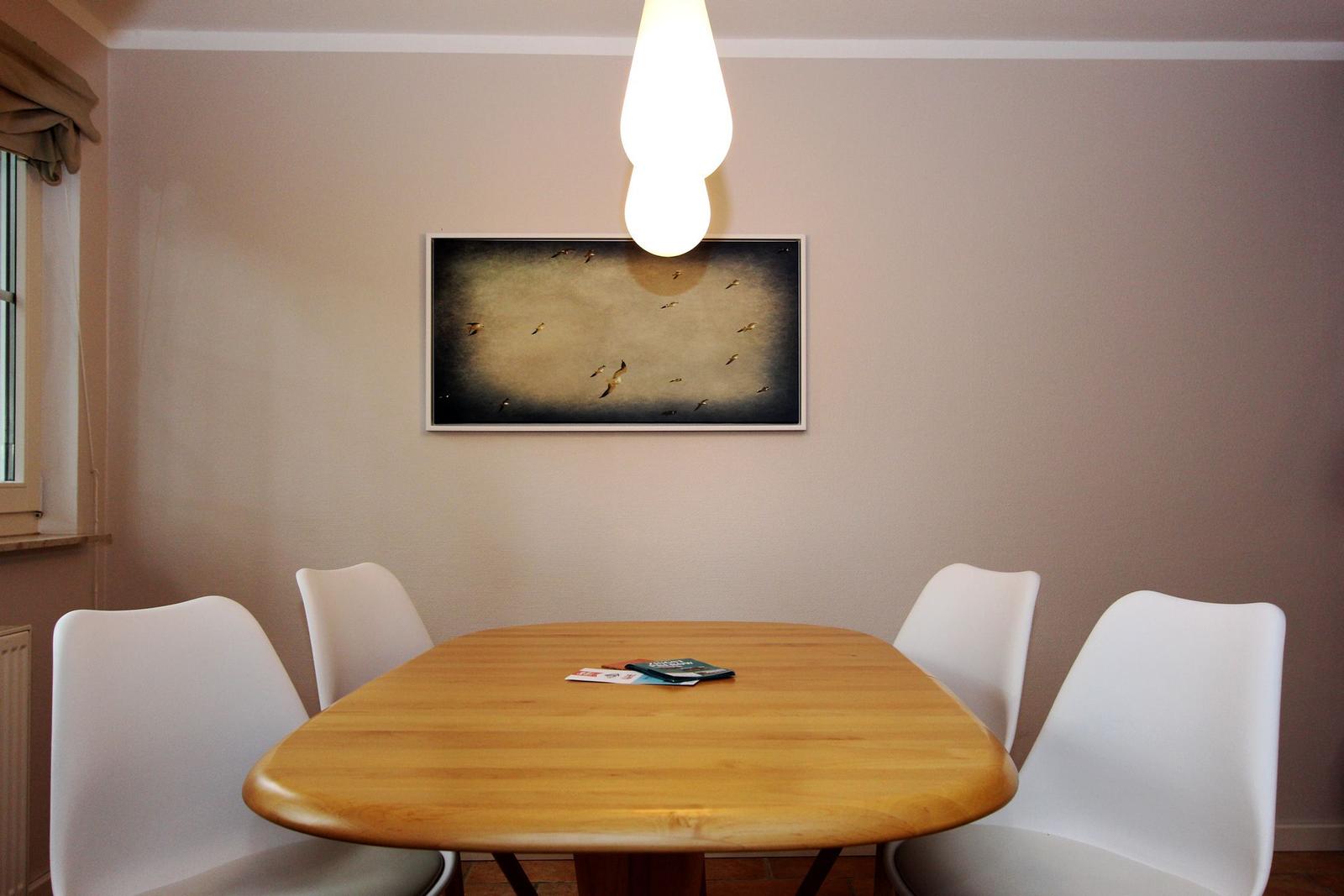 Esszimmer mit Holztisch, vier weißen Stühlen und Wandbild mit Vögeln.