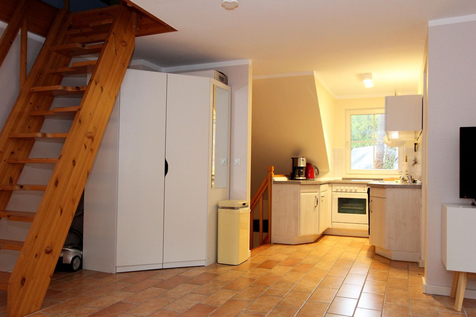 Küche mit Fenster, Holztreppe und Schrank. Fliesenboden und weißer Kühlschrank.