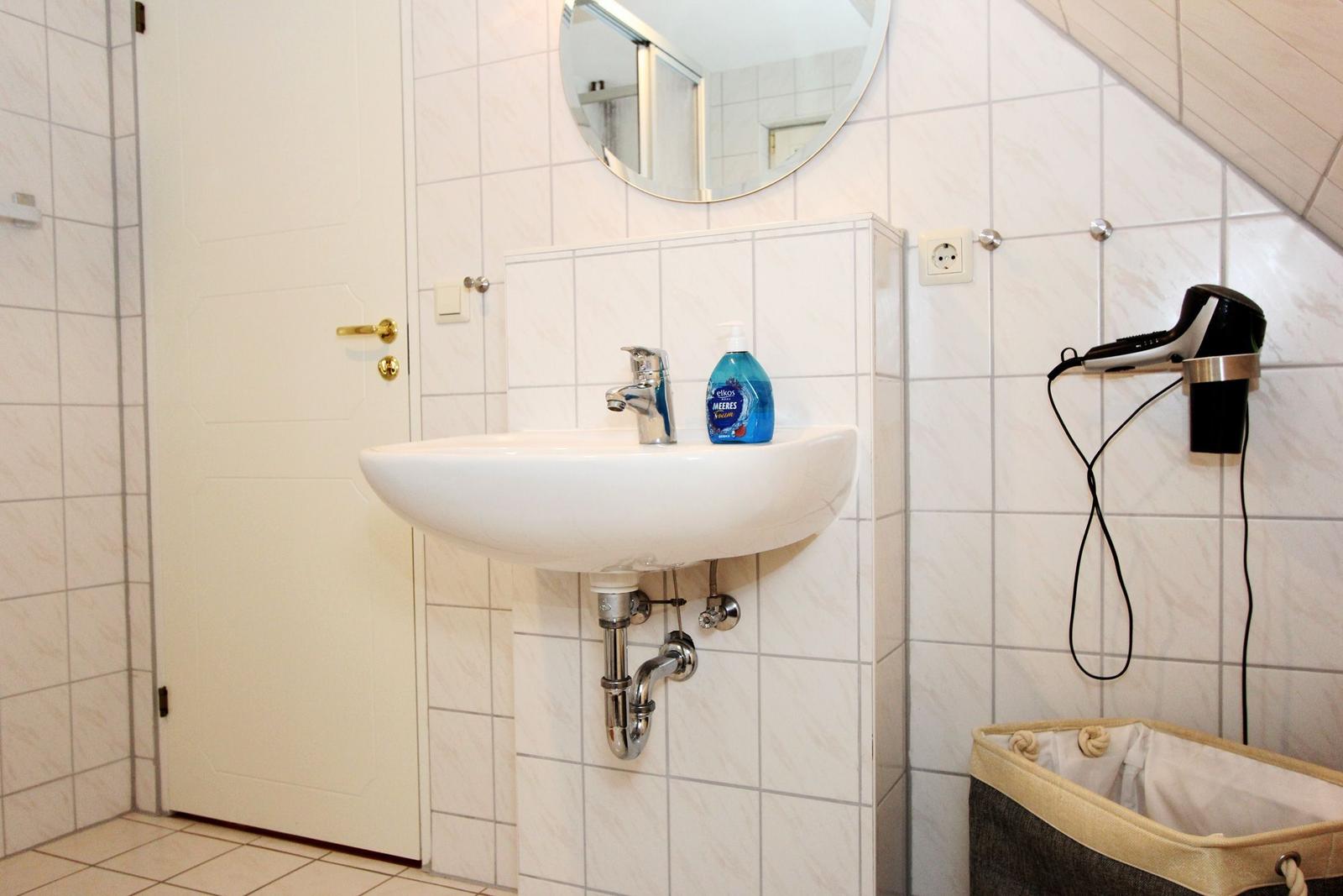 Bad mit Waschbecken, Spiegel und Handtuchhalter an der Wand.