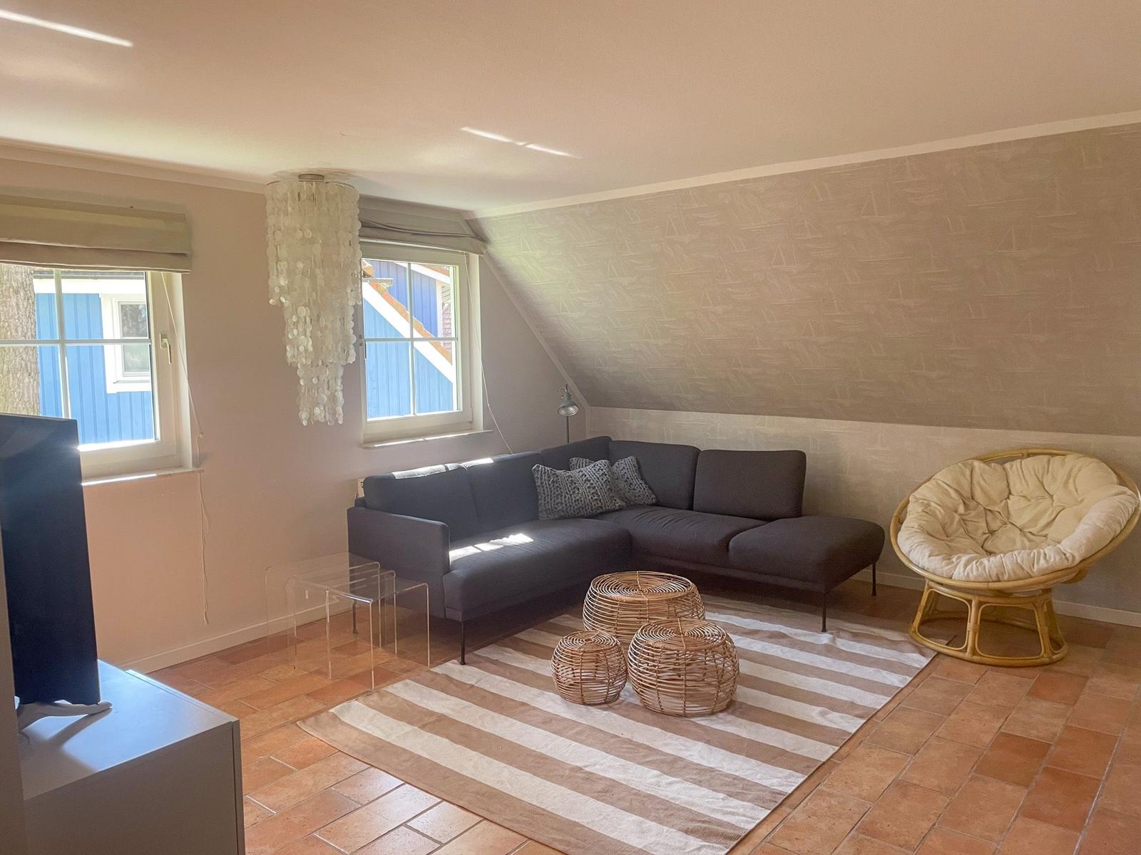 Wohnzimmer mit Sofa, Rattanmöbeln und Fenstern.
