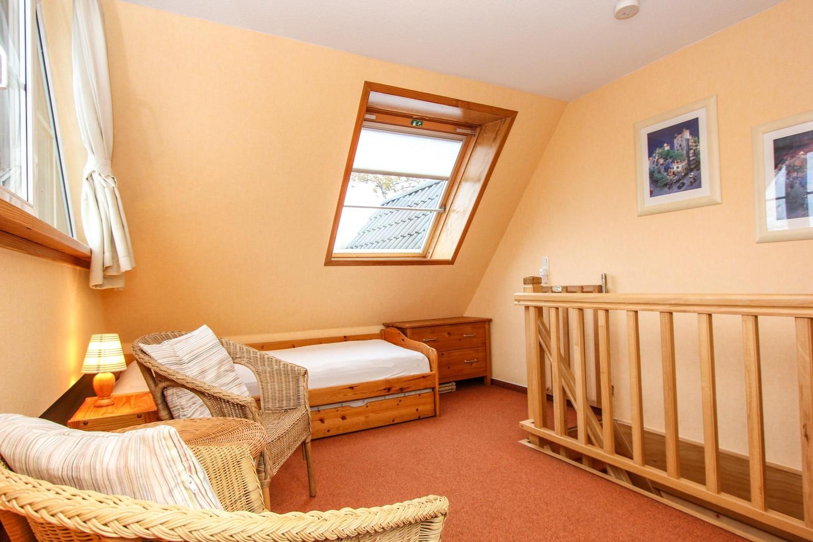 Schlafzimmer mit Dachschräge, Dachfenster, Holzbett und Wicker-Sessel.