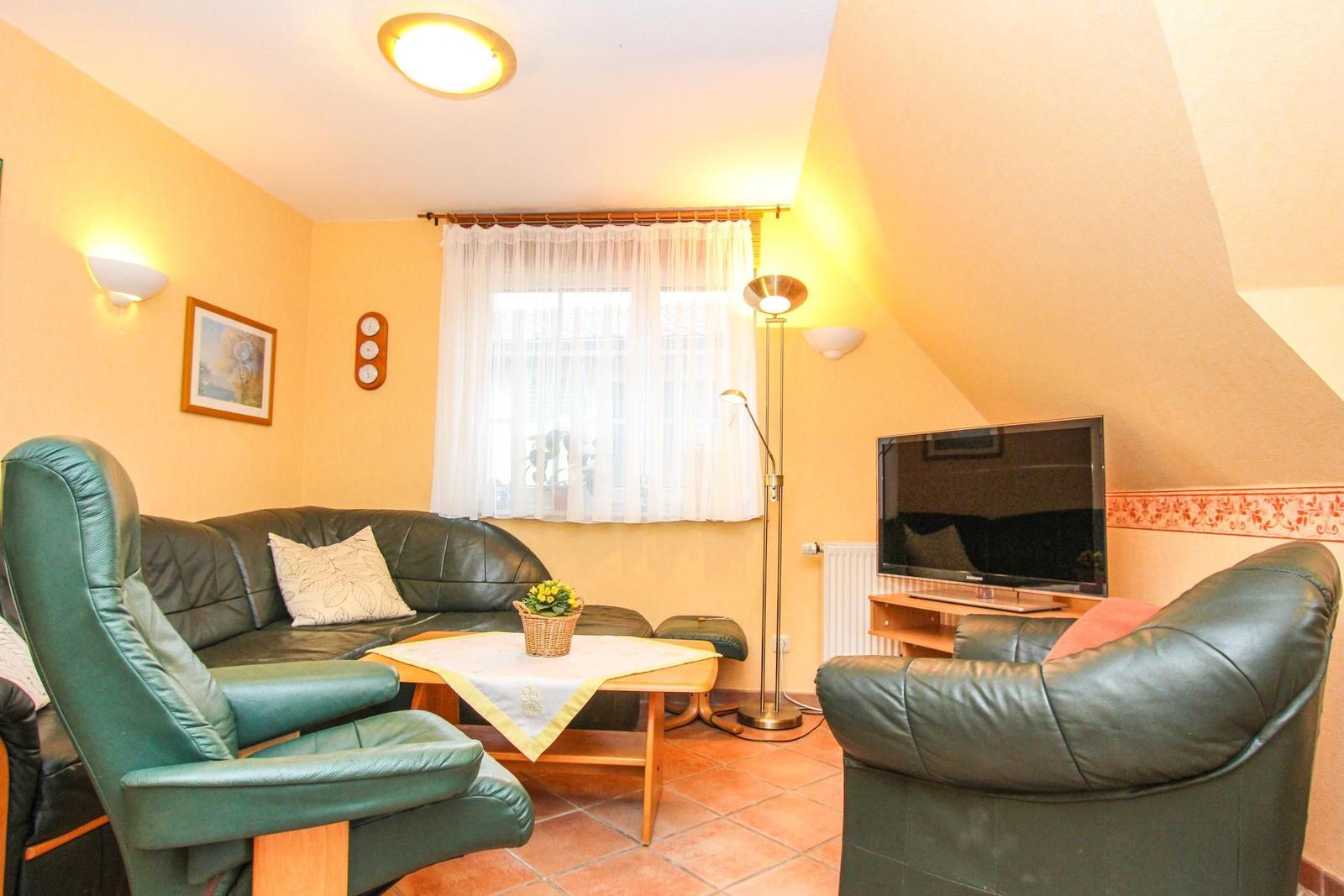 Wohnzimmer mit Sofa, Sessel, Fernseher und Tisch.