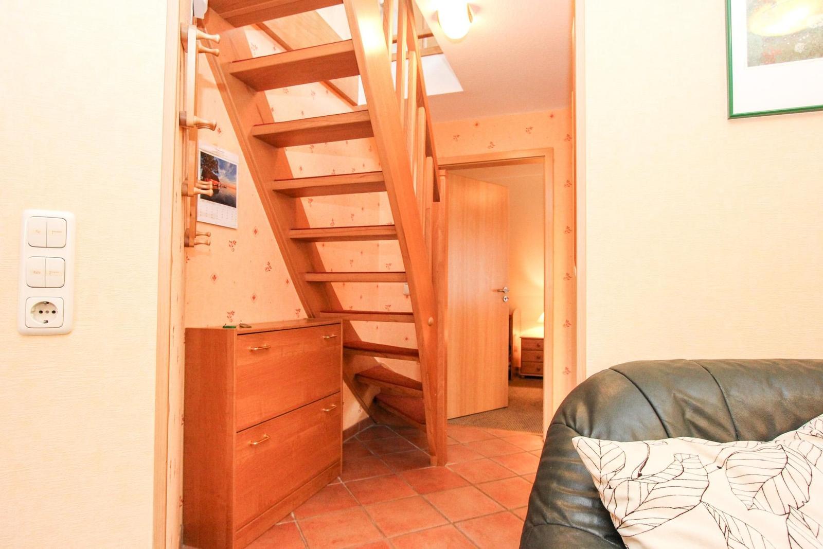 Treppenhaus mit Holztreppe, Schrank und Couch im Vordergrund.