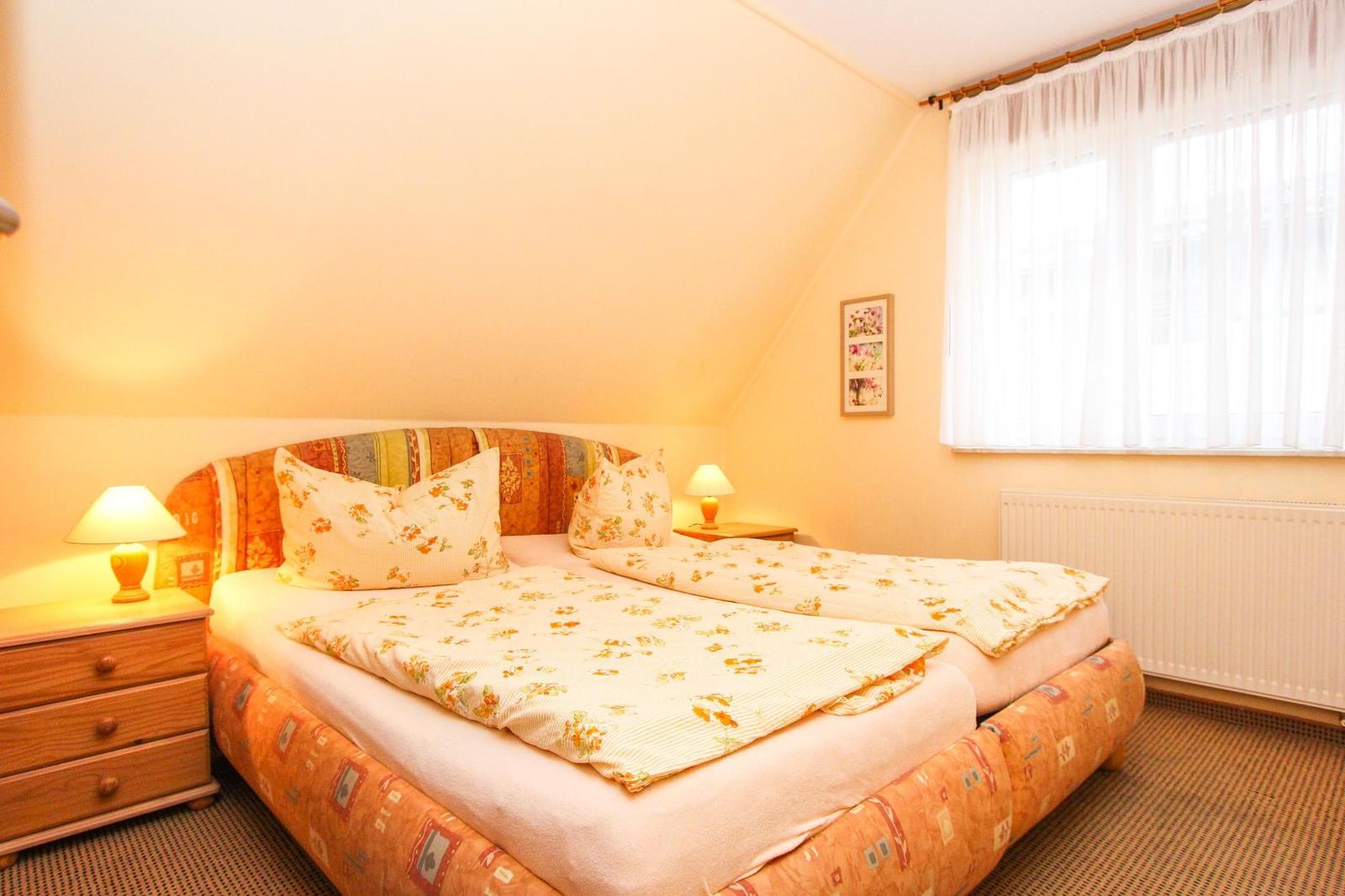 Doppelbett mit floraler Bettwäsche, Nachttische und Fenster mit Vorhängen.