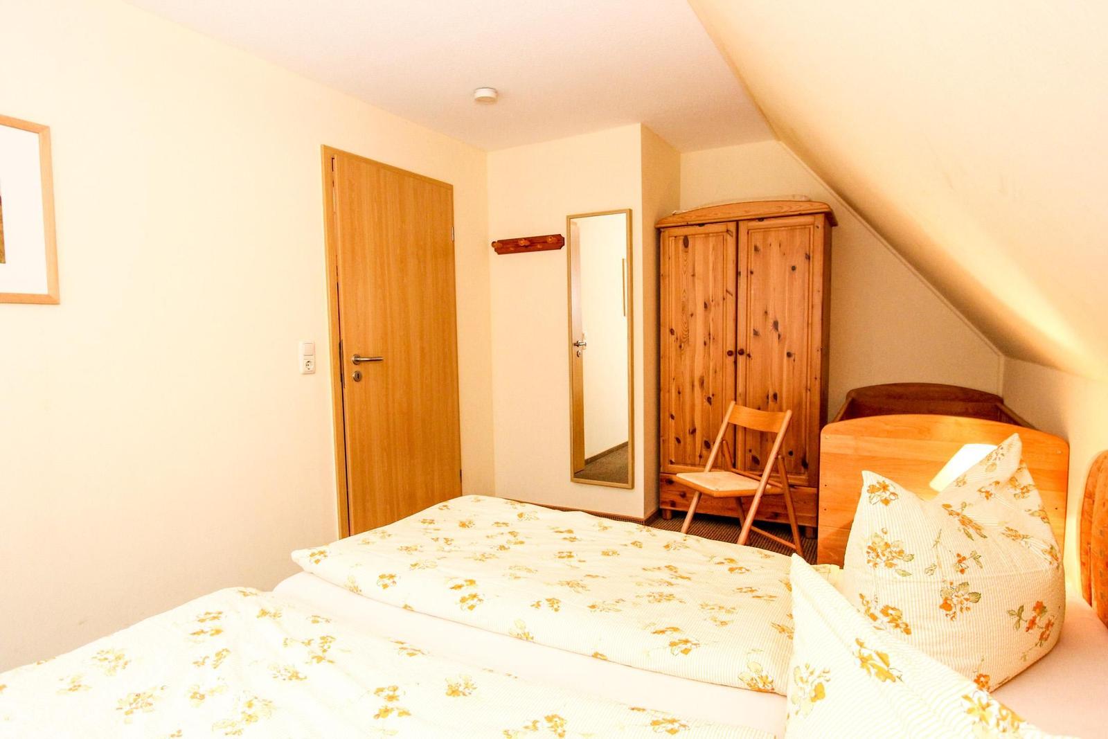 Schlafzimmer mit Bett, Kleiderschrank und Spiegel unter Dachschräge.