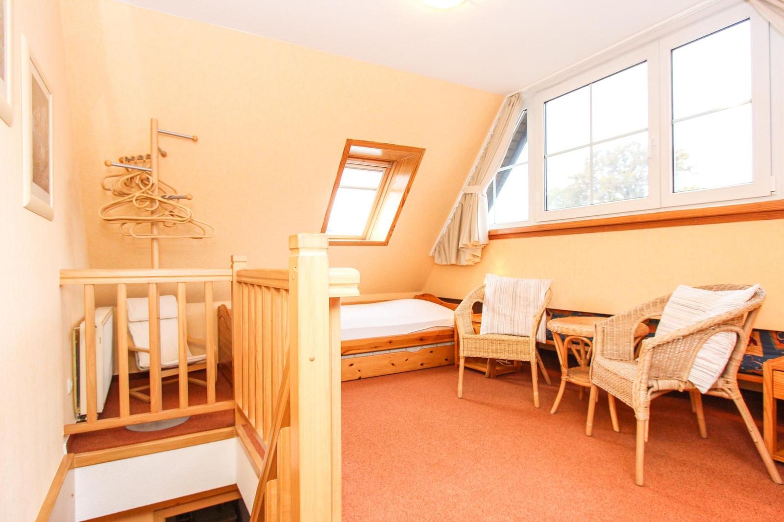 Dachgeschosszimmer mit Schlafcouch, zwei Stühlen und großem Fenster.