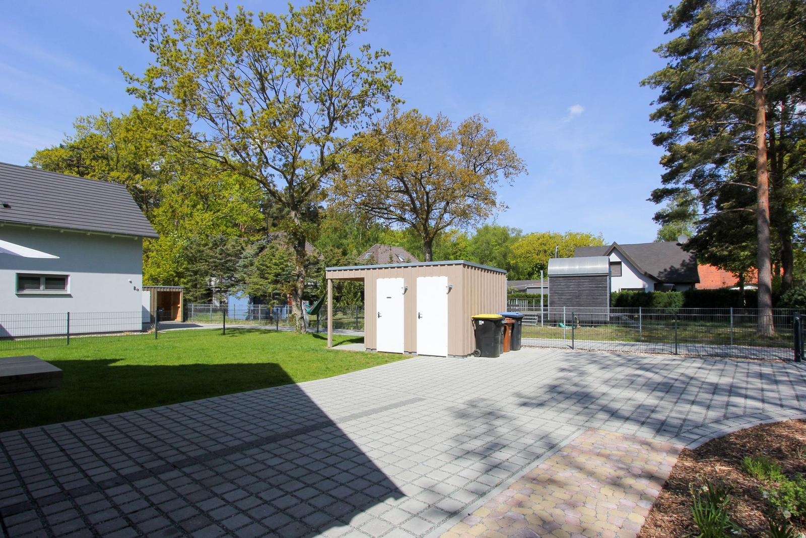 Hinterhof mit Pavillon, Mülltonnen und Grünfläche. Wohnhaus und Bäume im Hintergrund.