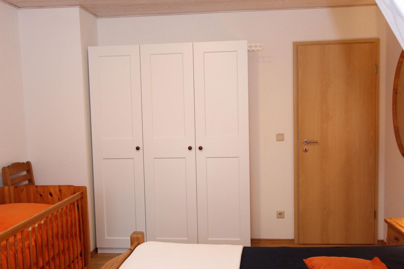 Schlafzimmer mit weißen Schrank, Holztür und Kinderbett mit orangefarbenem Bettzeug.