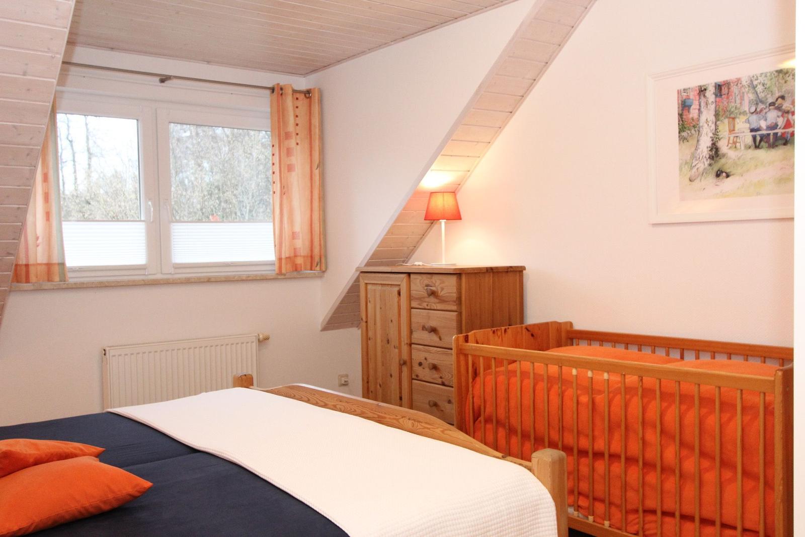 Schlafzimmer mit Babybett, Holzkommode und Fenster mit Blick auf Wald.
