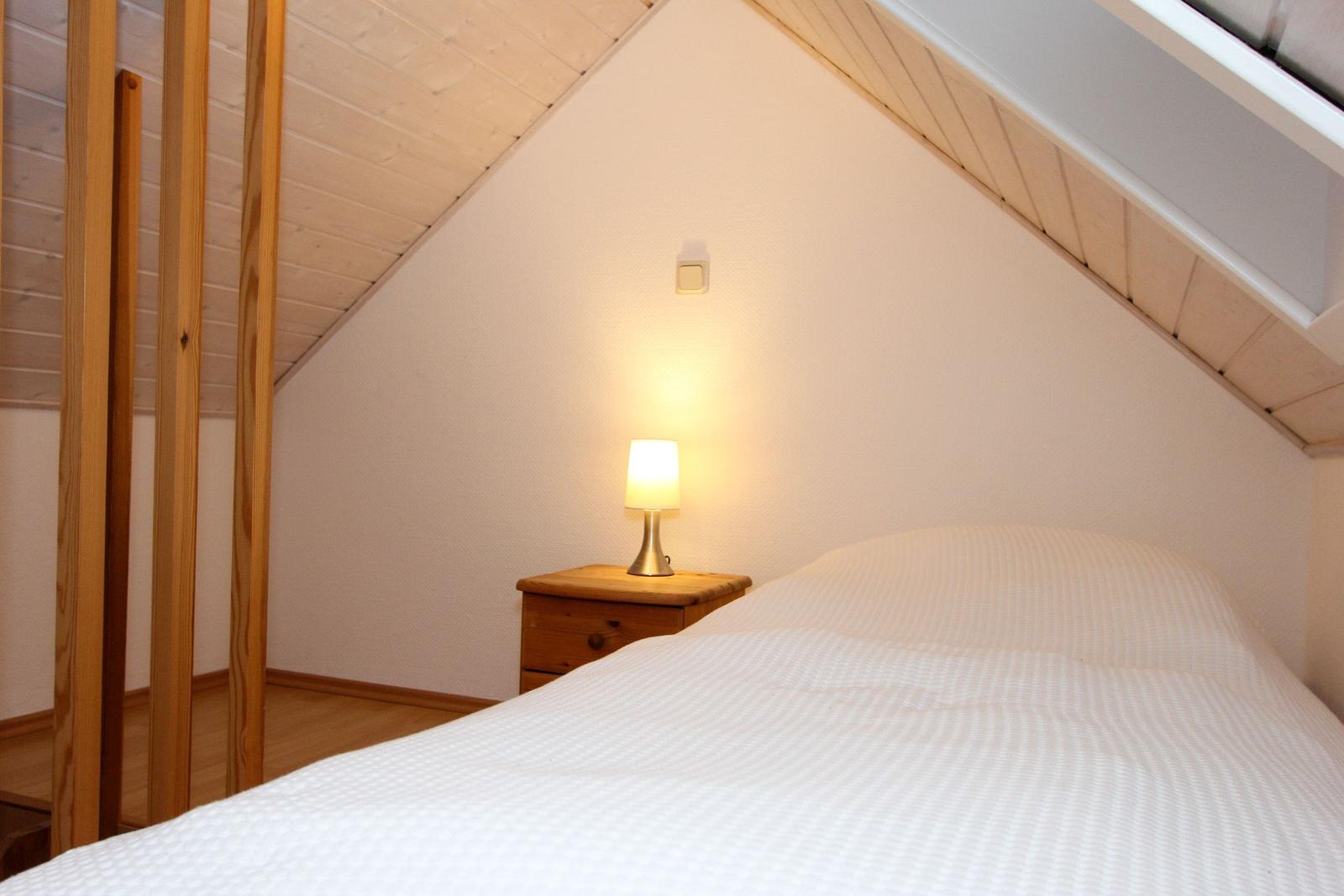 Schlafzimmer mit Dachschrägen, Bett und Nachttisch mit Lampe.